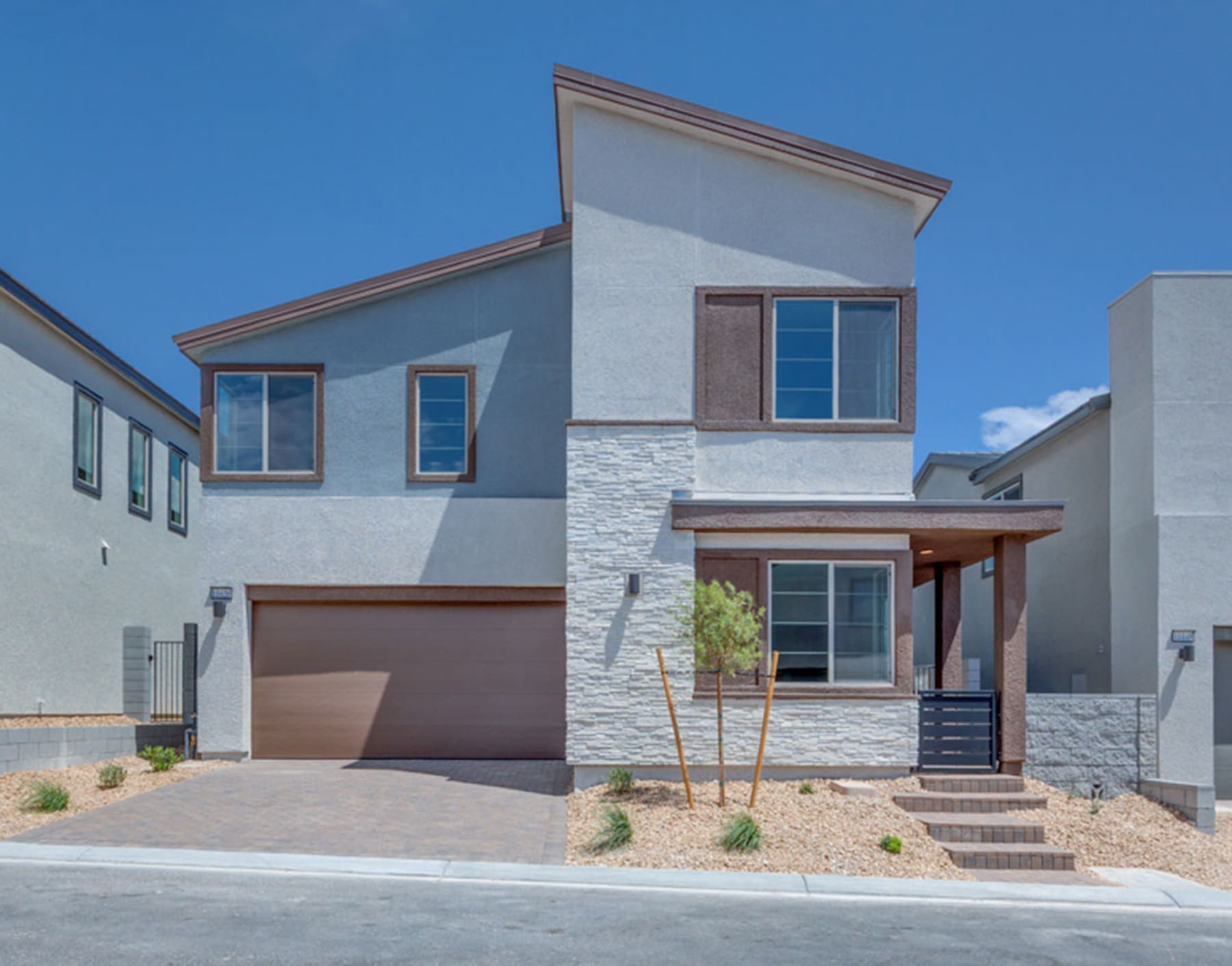 A modern two-story house with a stone facade, a garage door, and a covered porch, set against a clear blue sky.
