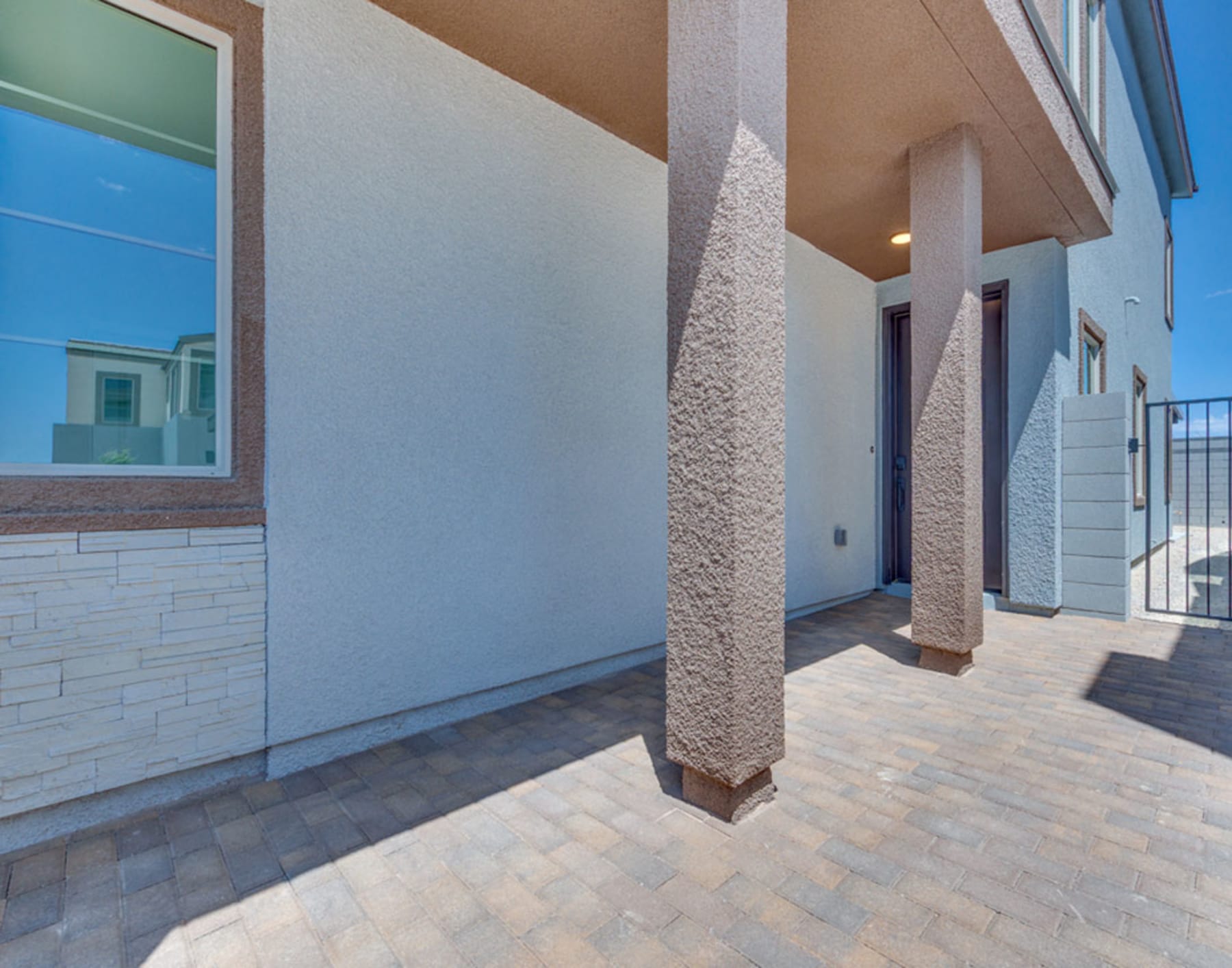 The image shows a modern, multi-story building with a textured exterior wall and a paved walkway leading to the entrance. The sky in the background appears to be a bright, clear blue.