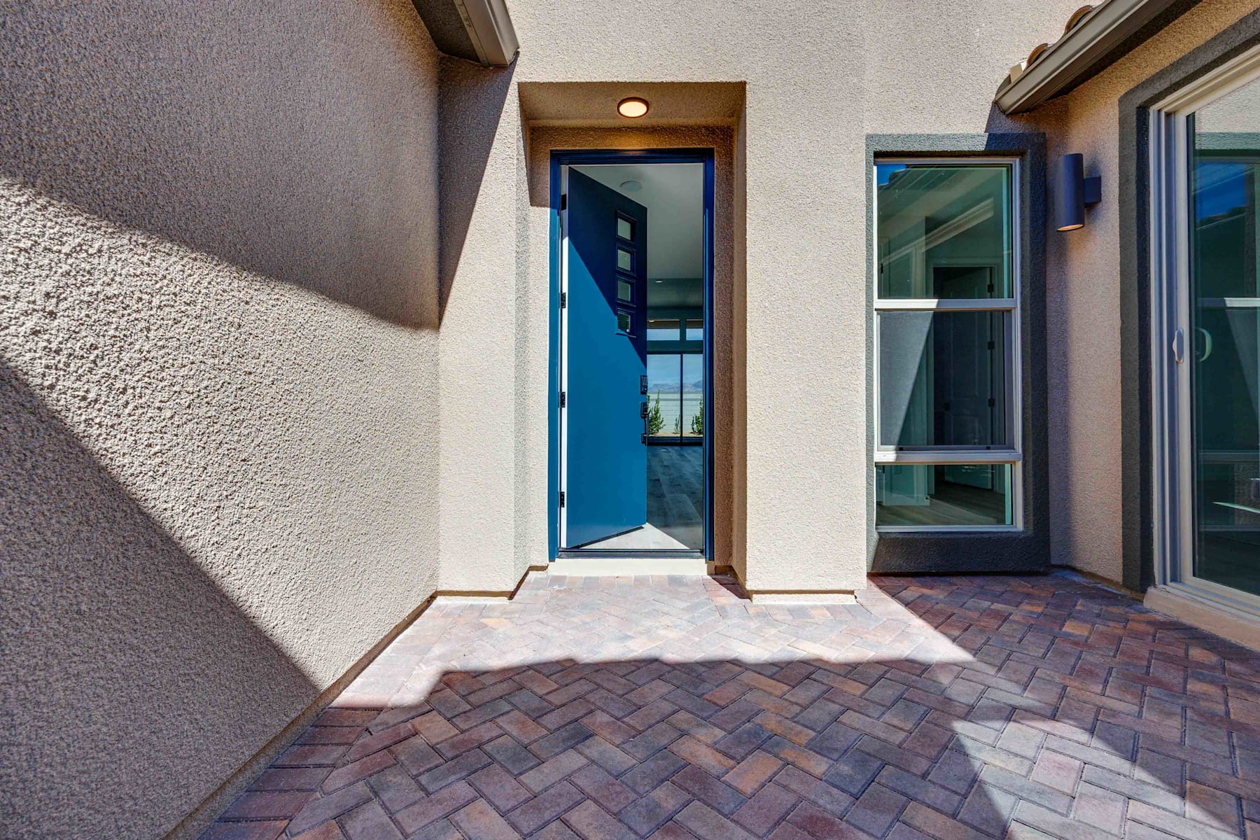 A brick-paved entryway leads to a glass-paneled door, with a wall-mounted light fixture and a textured exterior wall visible in the background.