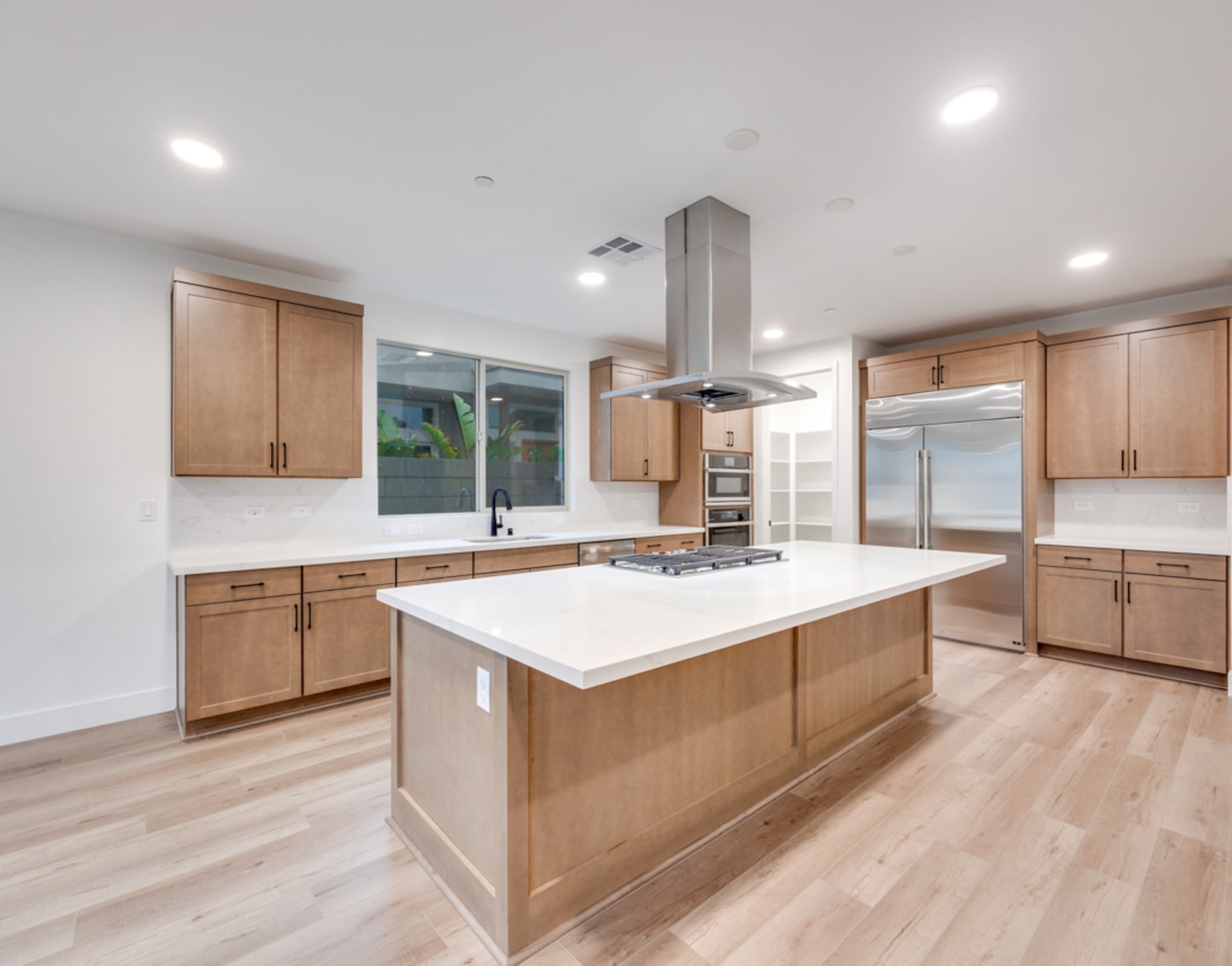 A modern, open-concept kitchen with light wood cabinets, a large island with a white countertop, and hardwood flooring.