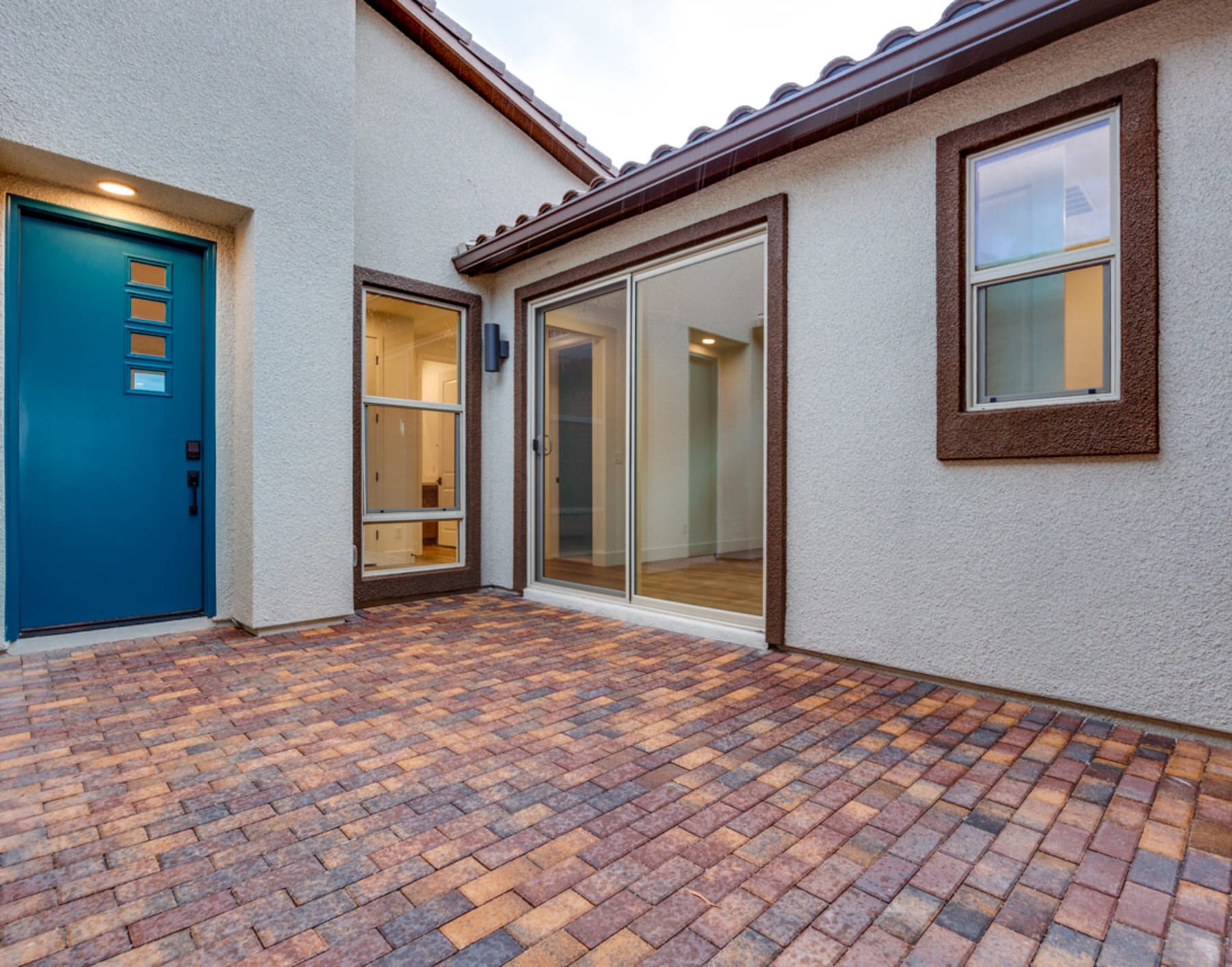 The image shows a modern, well-designed exterior of a building with a blue door, large windows, and a brick paved walkway leading to the entrance.