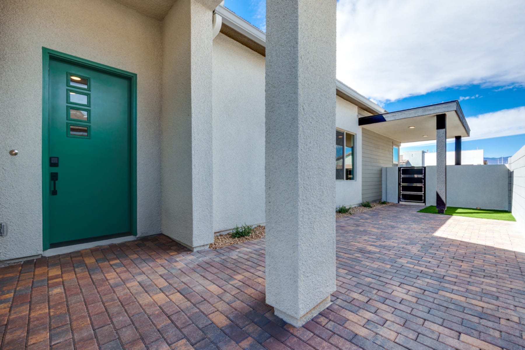 A modern, minimalist exterior with a green door, brick paving, and a clear sky in the background.