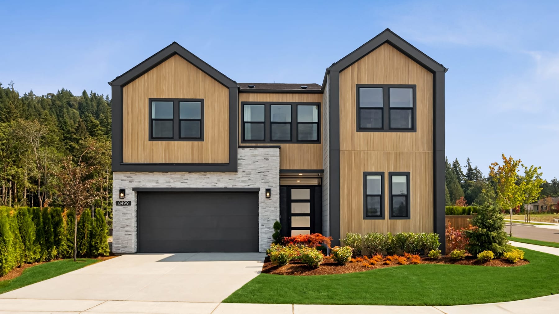 A modern two-story house with a garage, surrounded by a well-manicured lawn and lush greenery in the background.