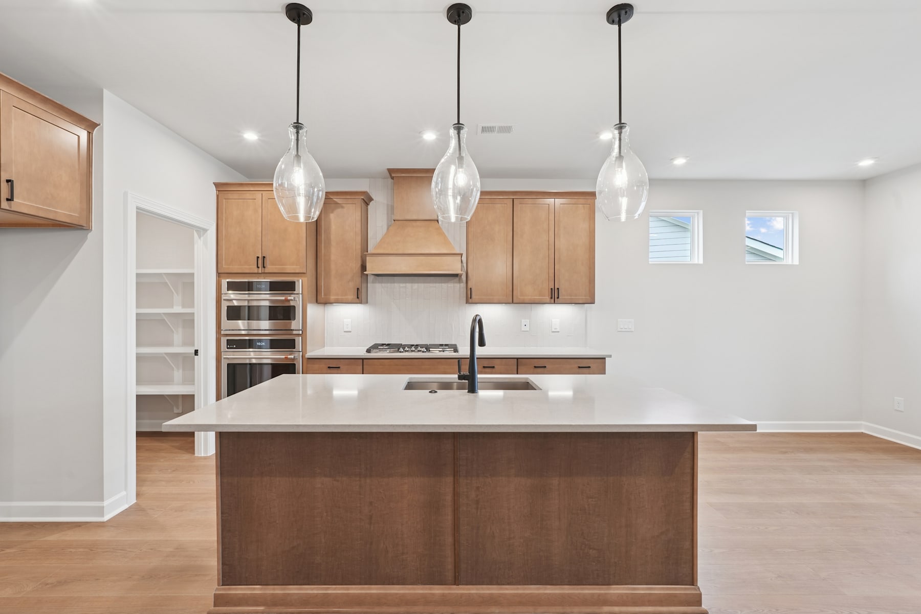 A modern, open-concept kitchen with light wood cabinets, a white countertop, and three pendant lights hanging above the island.