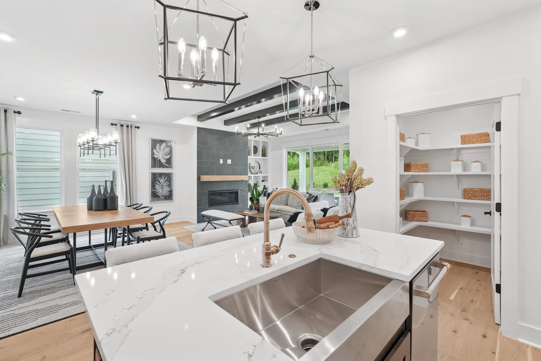 A modern, open-concept kitchen with a large stainless steel sink, wooden countertops, and a dining area with a long table and chairs in the background.