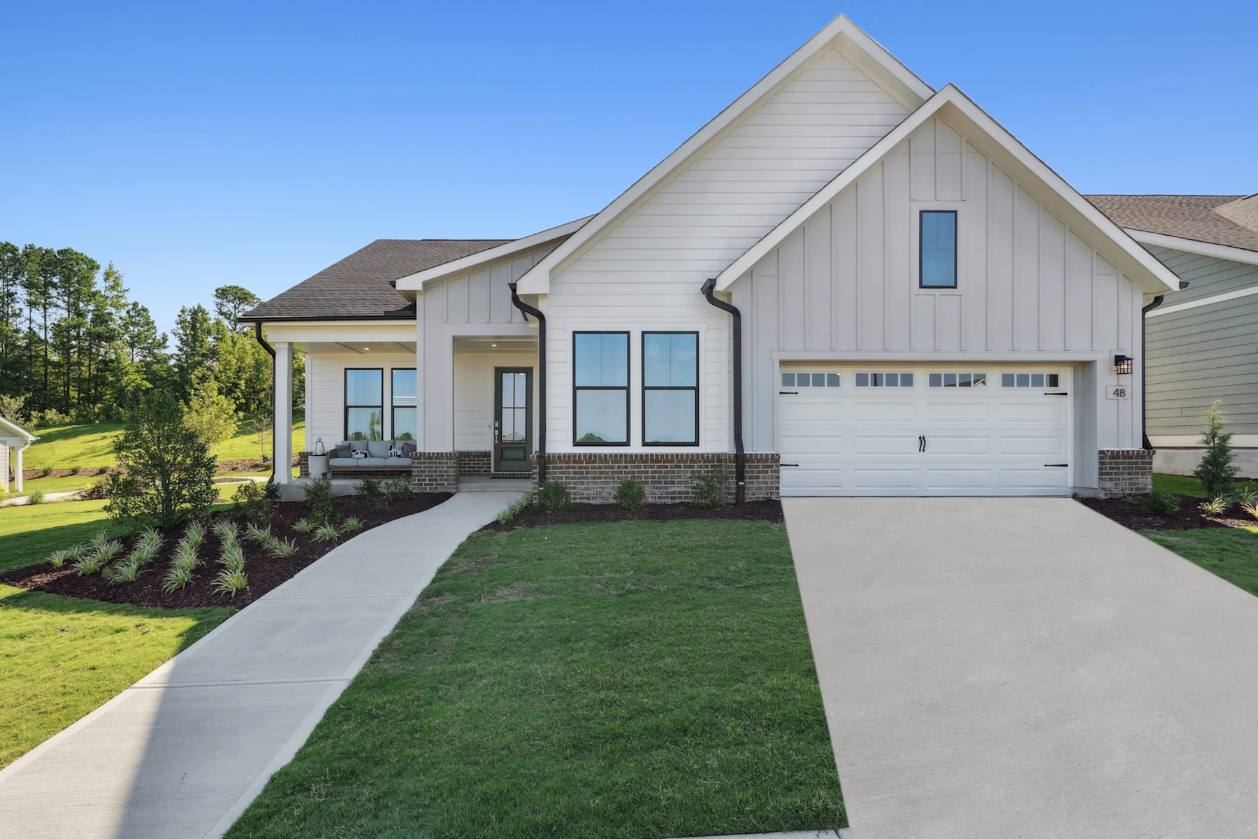 A modern, two-story house with a white exterior, a gabled roof, and a well-manicured lawn in the foreground, set against a backdrop of lush greenery and a clear blue sky.