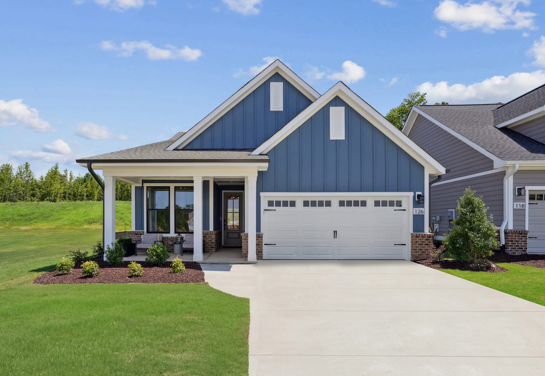 A modern two-story house with a gray exterior, a garage, and a well-manicured lawn surrounded by trees in the background.