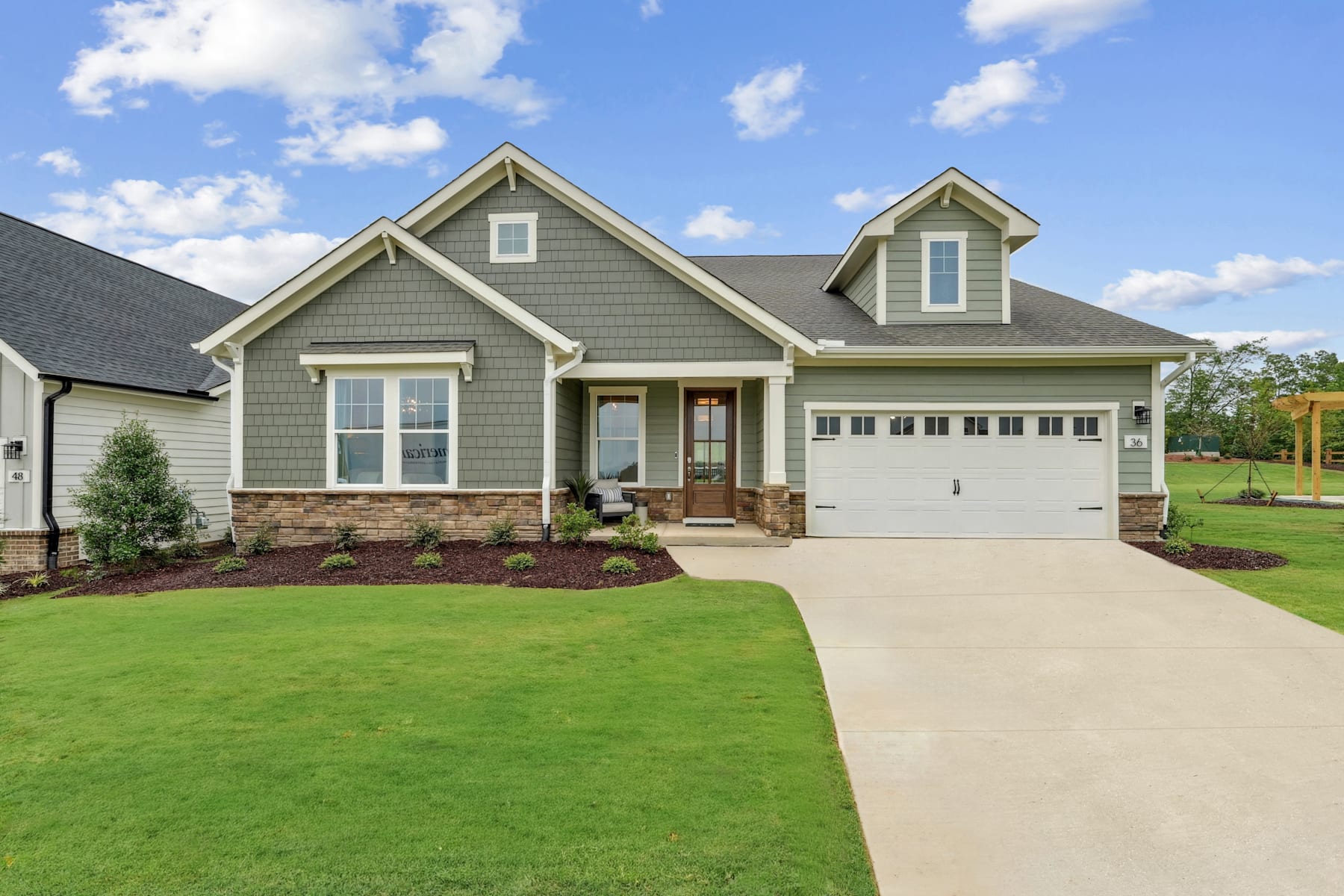 A well-maintained two-story house with a gray exterior, a garage, and a neatly landscaped yard with a lush green lawn in the foreground, set against a blue sky with fluffy white clouds.