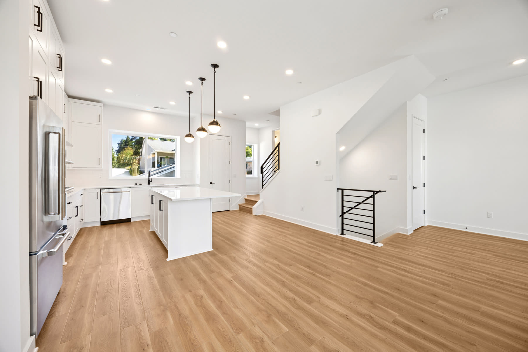 A modern, open-concept kitchen and living space with white walls, hardwood floors, and pendant lighting fixtures.