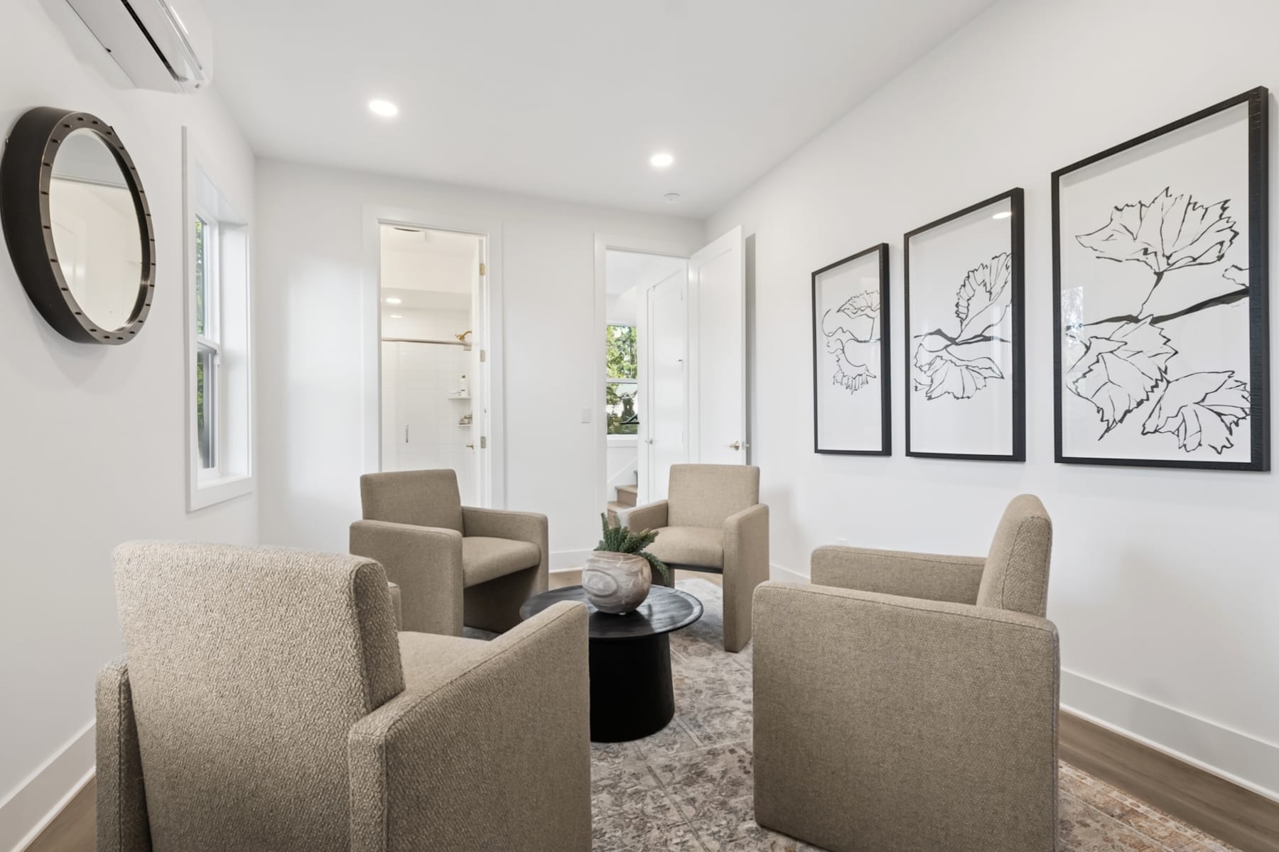 A modern and minimalist living room with beige armchairs, a round coffee table, and framed botanical prints on the walls, creating a serene and inviting atmosphere.