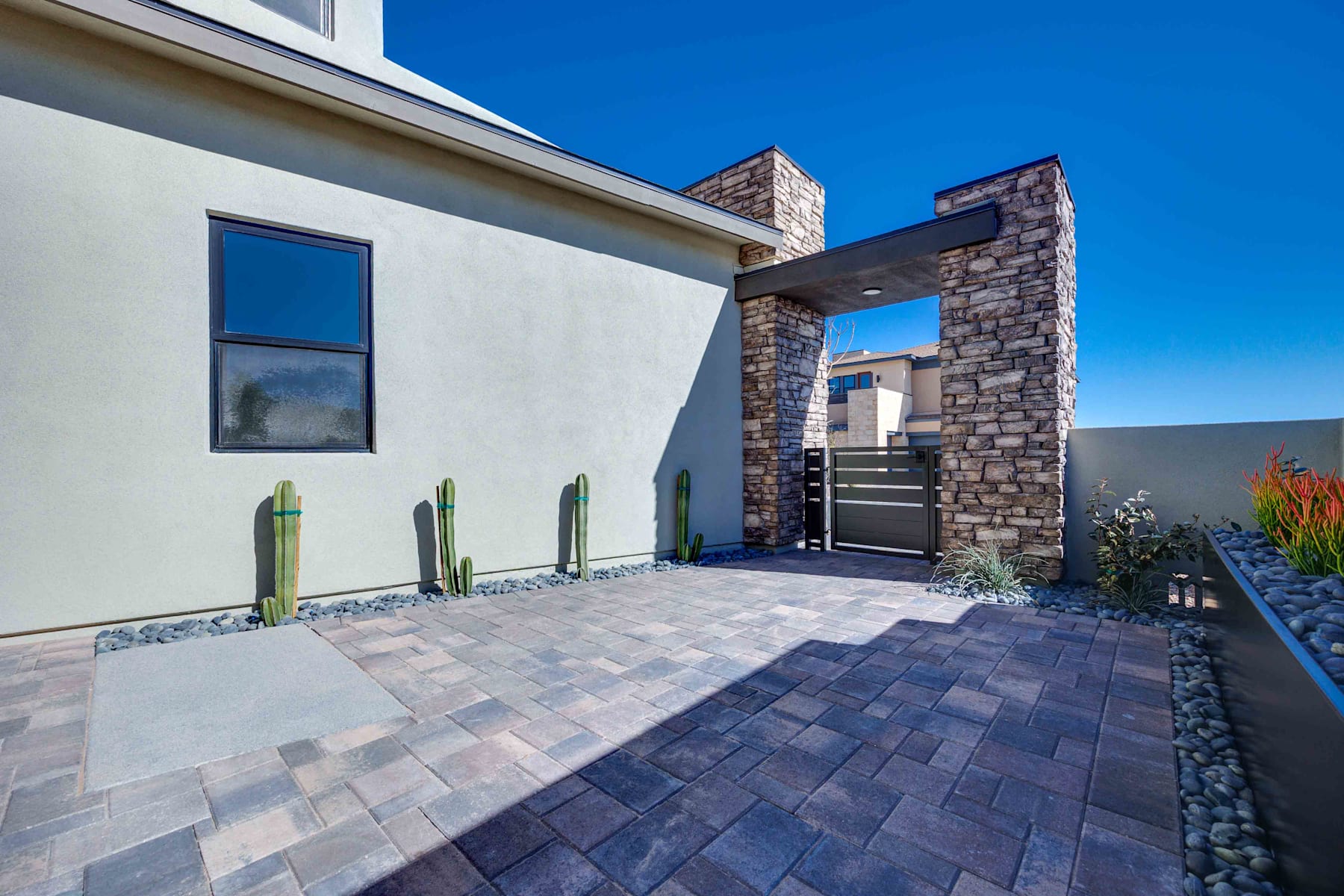 A modern, two-story house with a stone and stucco exterior, a paved walkway leading to the entrance, and a clear blue sky in the background.