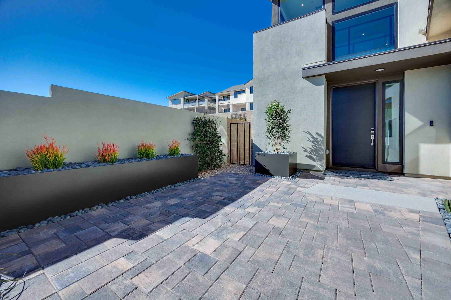A modern, well-designed exterior with a paved walkway, potted plants, and a sleek, contemporary building in the background under a clear blue sky.