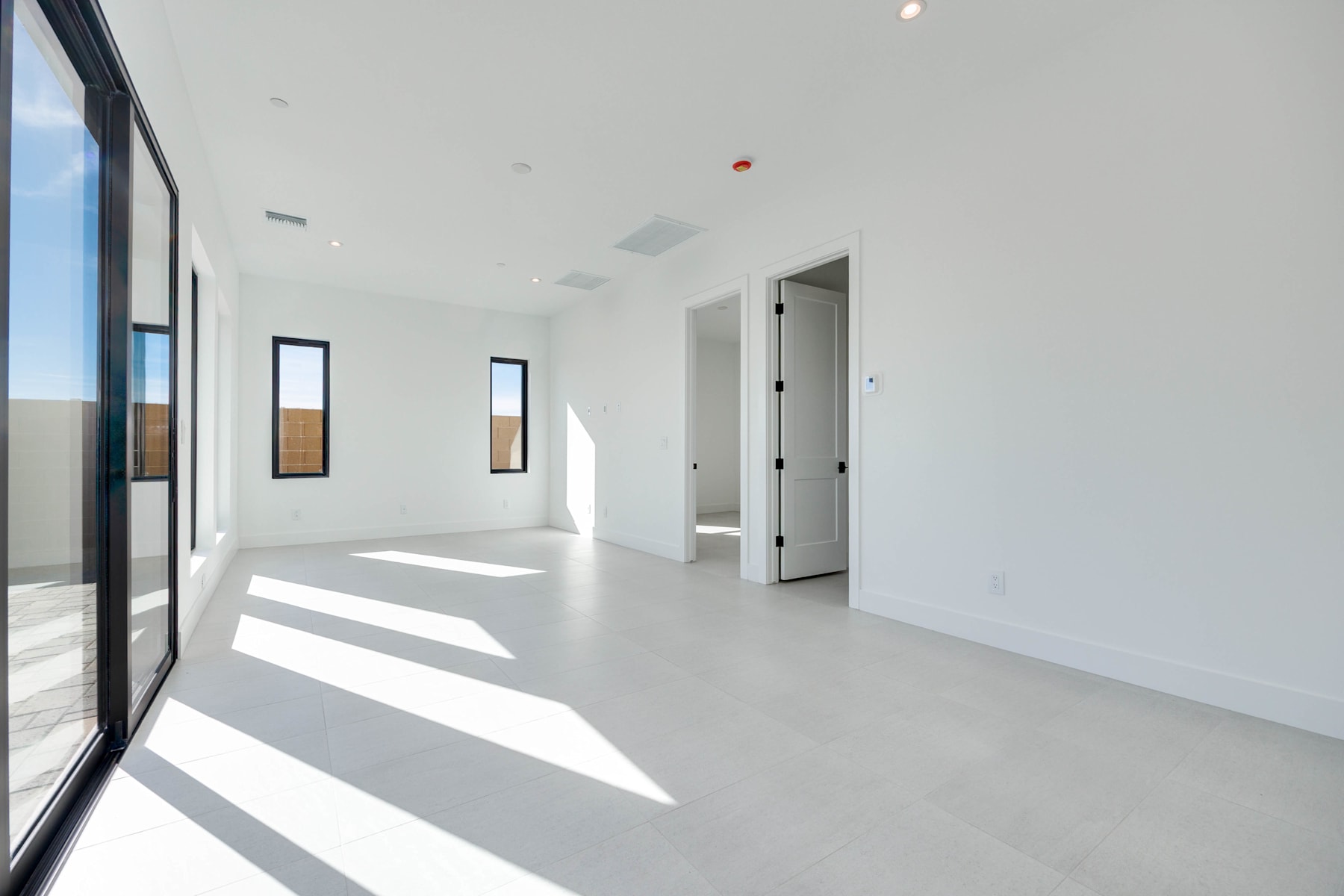 A spacious, minimalist interior with large windows, white walls, and a smooth, light-colored floor. The room appears to be well-lit, with natural light streaming in through the windows.