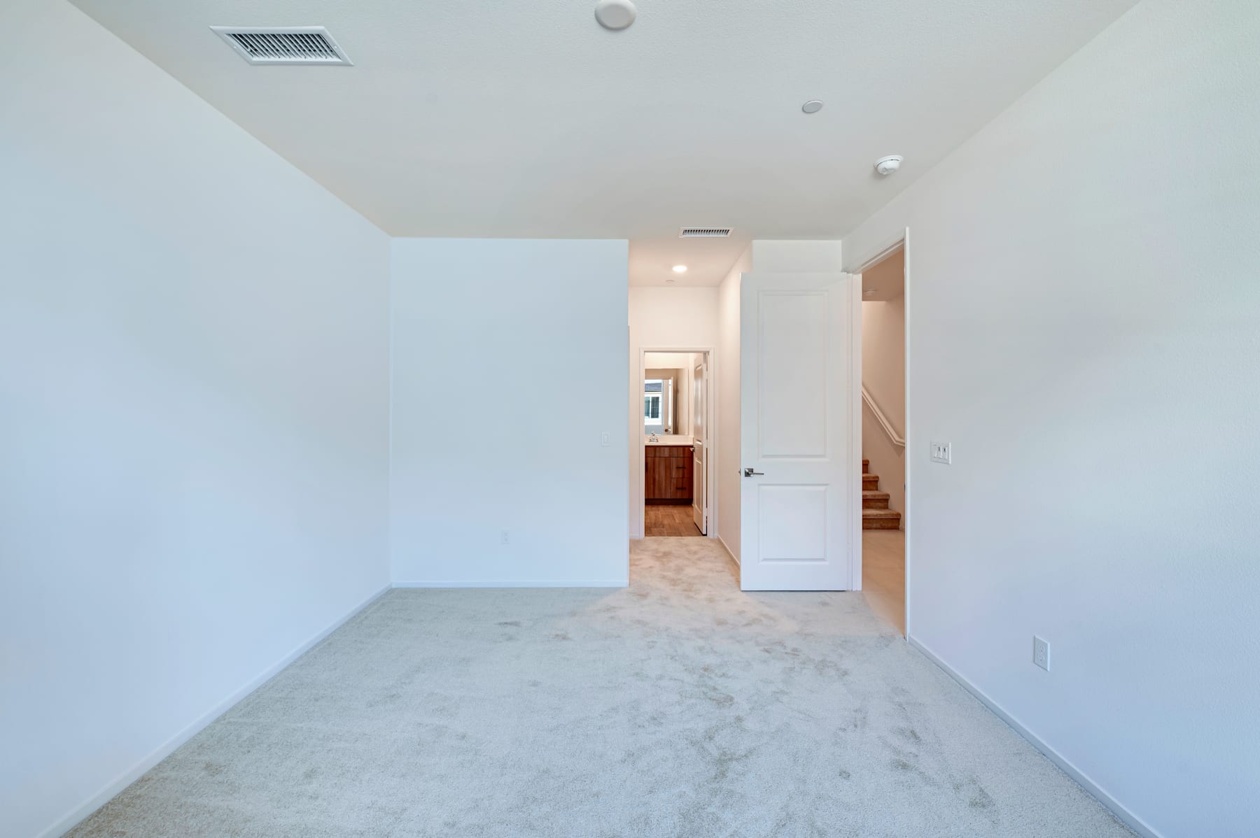 A spacious, minimalist room with white walls, a marble-like floor, and a doorway leading to another area.