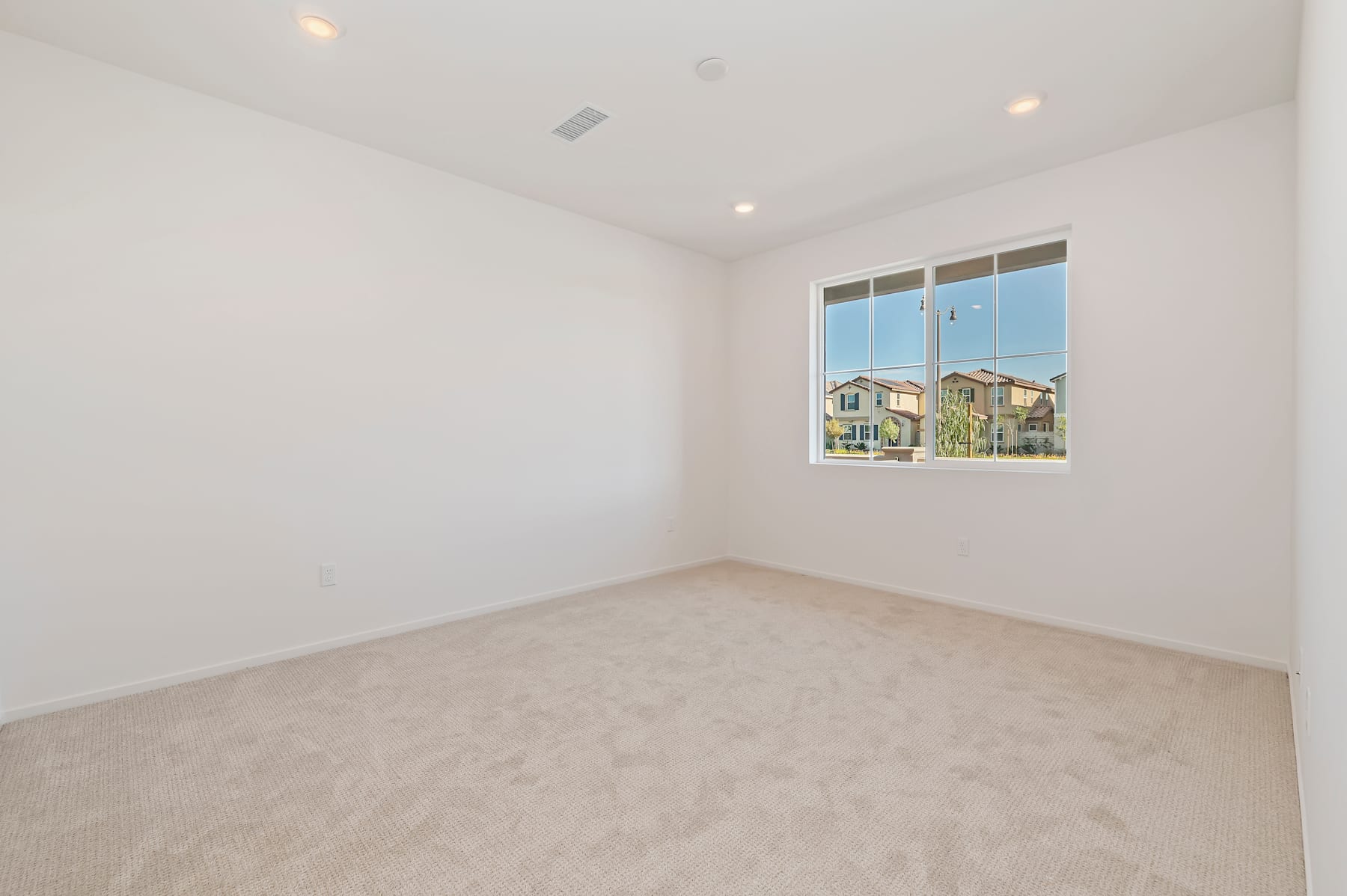 A spacious, well-lit room with a large window overlooking a residential neighborhood in the background.