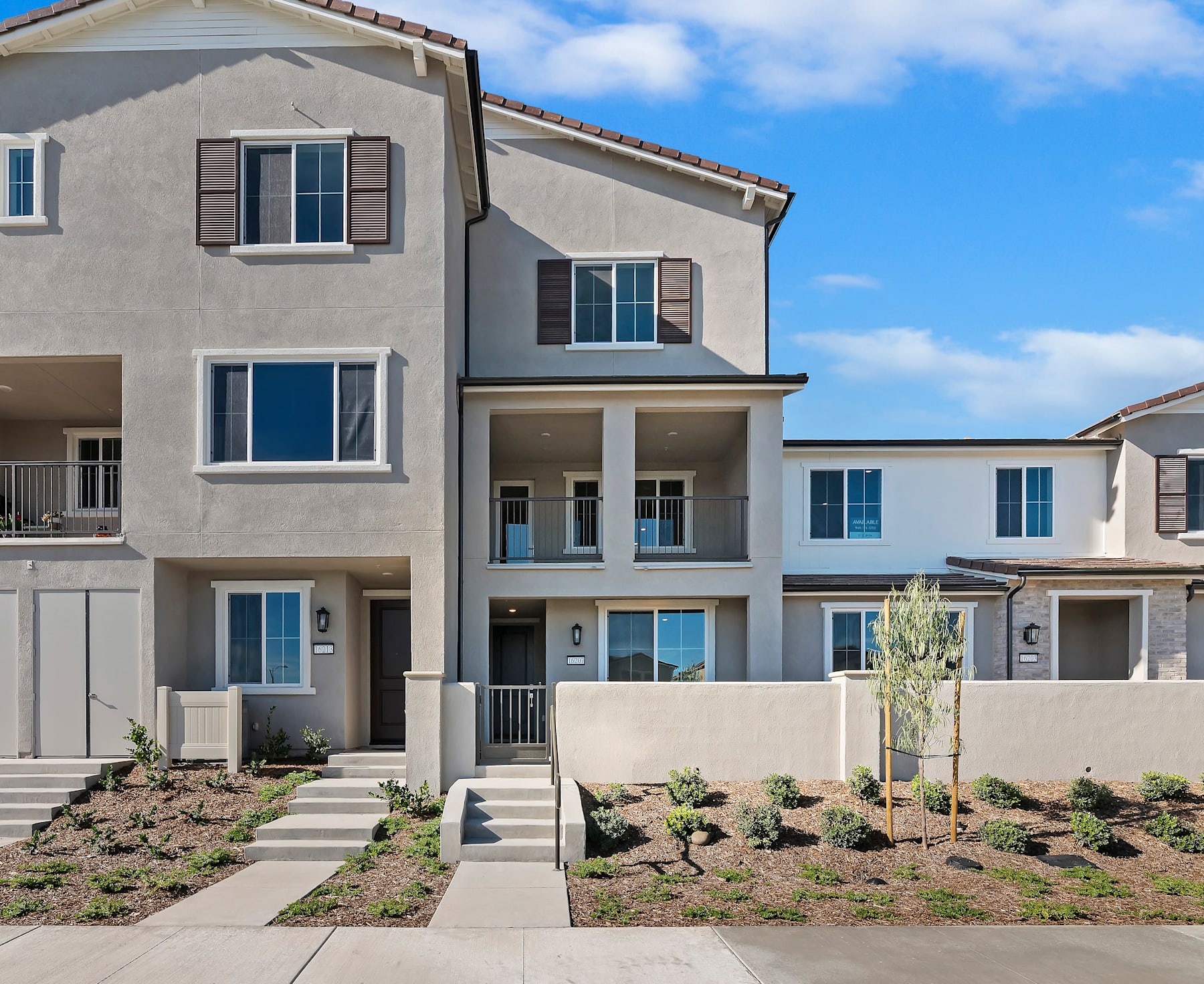 A modern, multi-story townhouse with a landscaped front yard and a clear blue sky in the background.