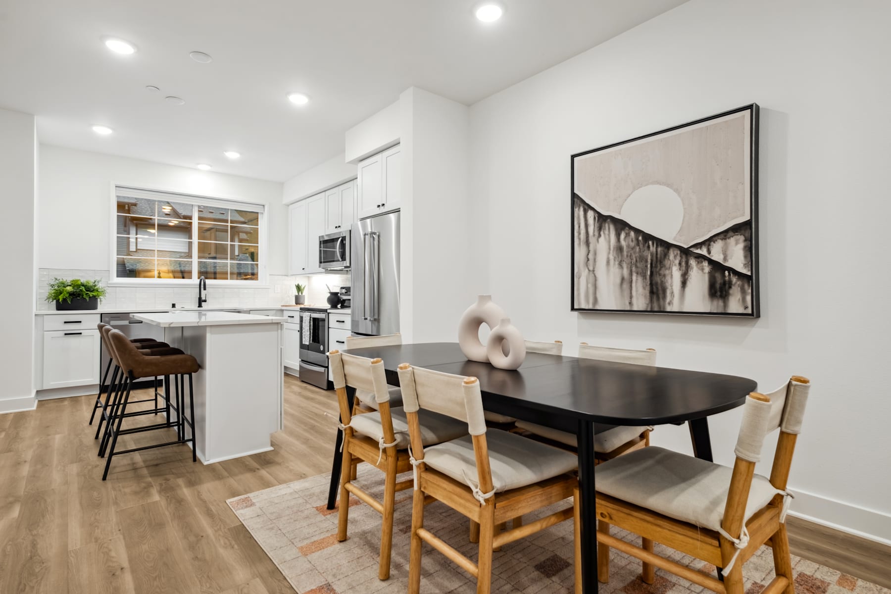 A modern and minimalist kitchen and dining area with a wooden dining table, chairs, and a large abstract artwork on the wall.