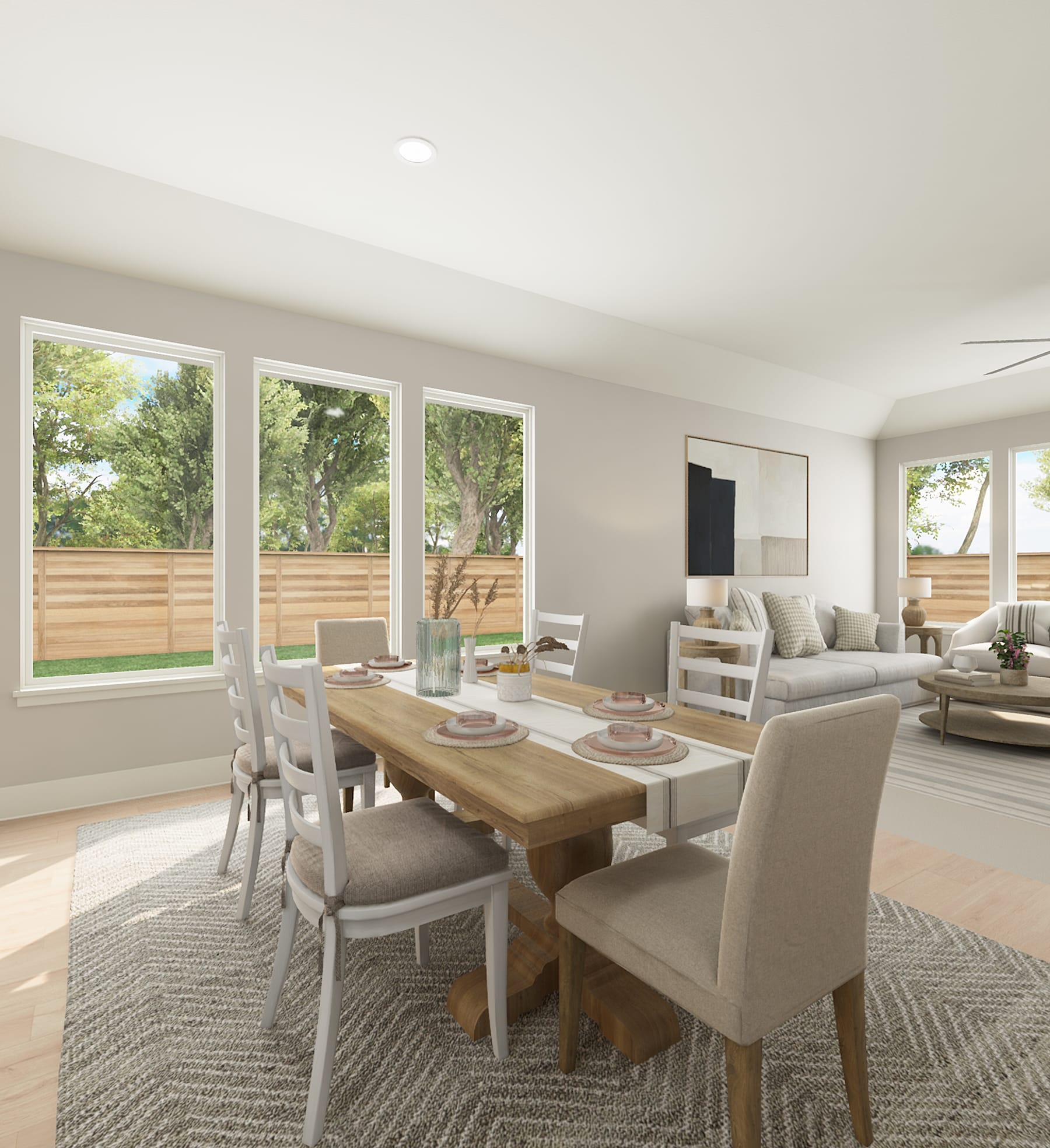 A spacious and well-lit open-plan living and dining area with a wooden dining table, upholstered chairs, and a comfortable sofa set against a backdrop of large windows overlooking a lush outdoor landscape.