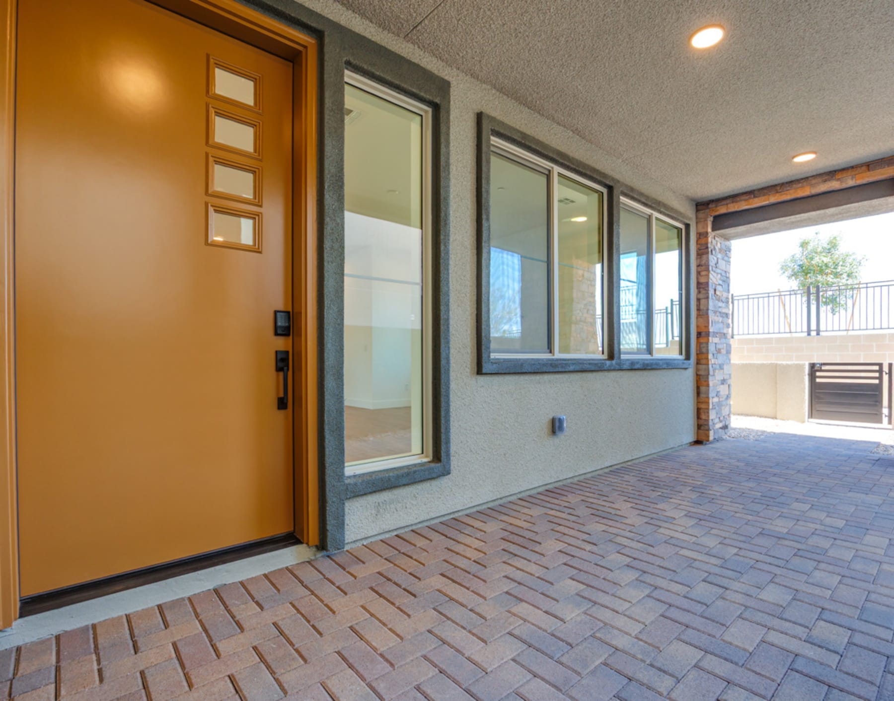 A modern entryway with a wooden door, large windows, and a brick paved floor leading to an outdoor area.