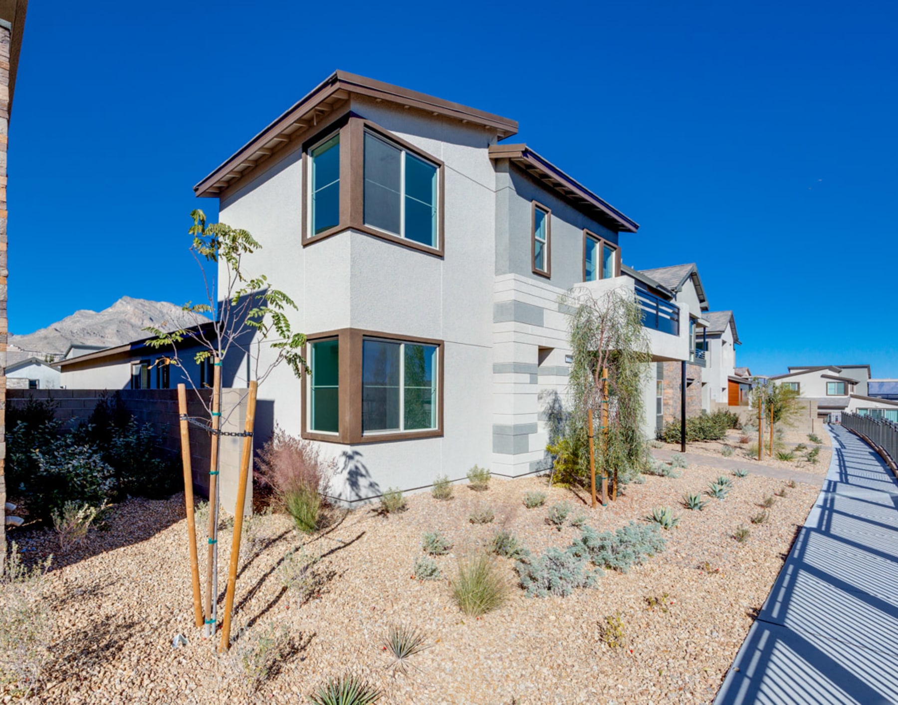 A two-story residential building with a desert-inspired landscape in the foreground, set against a clear blue sky.