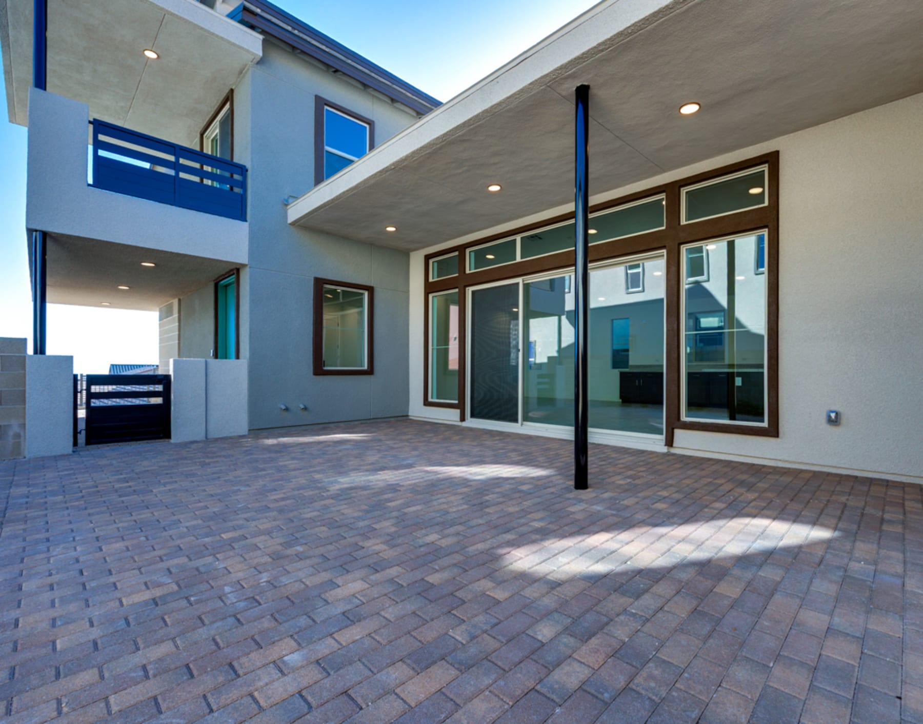 A modern, multi-story building with a paved courtyard in the foreground, featuring a mix of glass, concrete, and brick elements in shades of blue and gray.