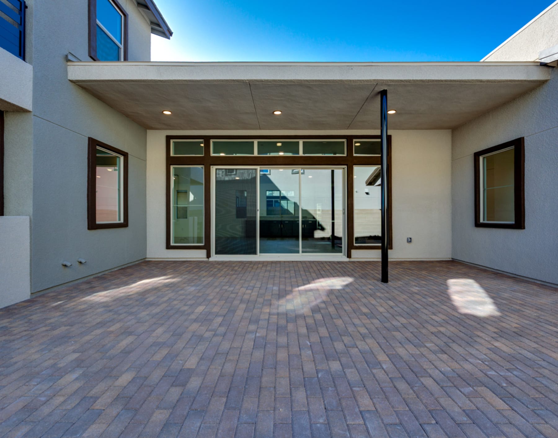A modern, two-story building with a covered entryway and a paved brick courtyard in the foreground, set against a clear blue sky.