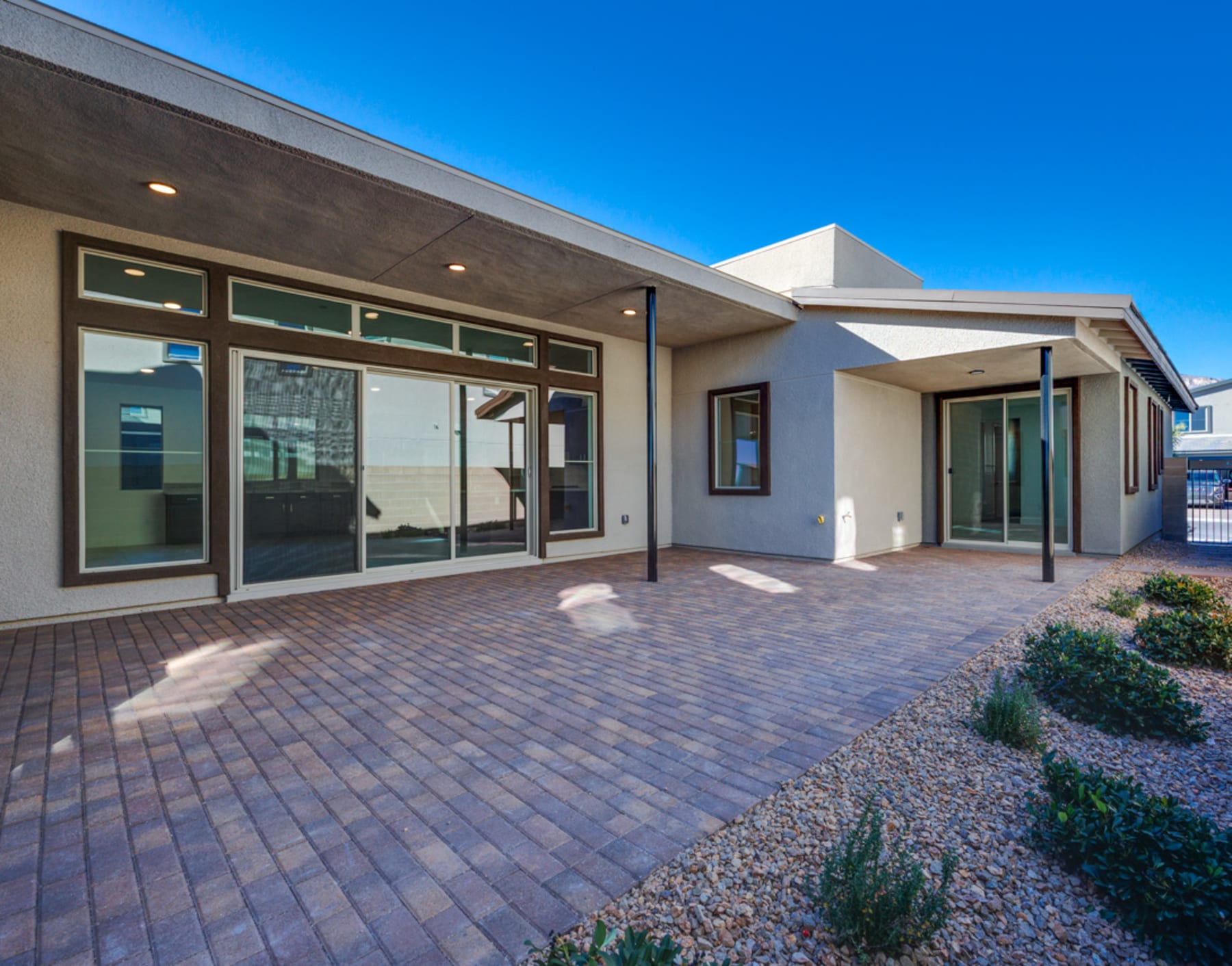 A modern, single-story building with a paved patio and landscaped surroundings, set against a clear blue sky.