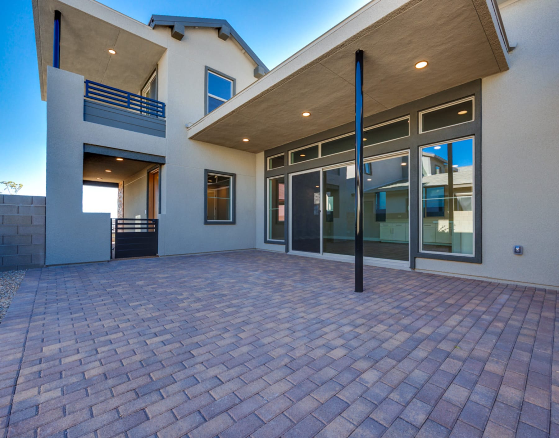 A modern, two-story residential building with a paved driveway and large windows in the foreground, set against a clear blue sky in the background.