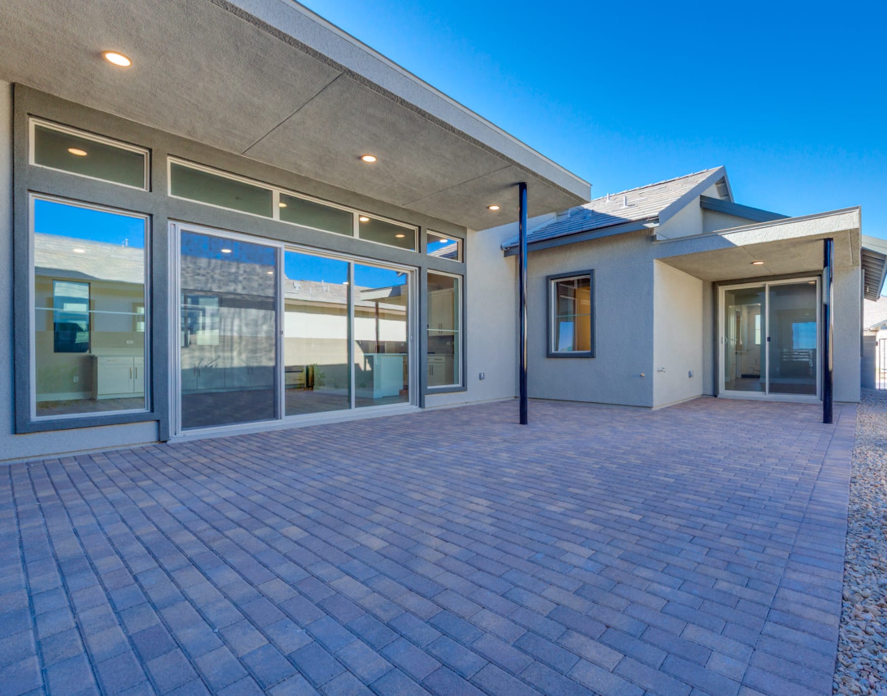 A modern, two-story building with large windows and a paved courtyard in the foreground, set against a clear blue sky.