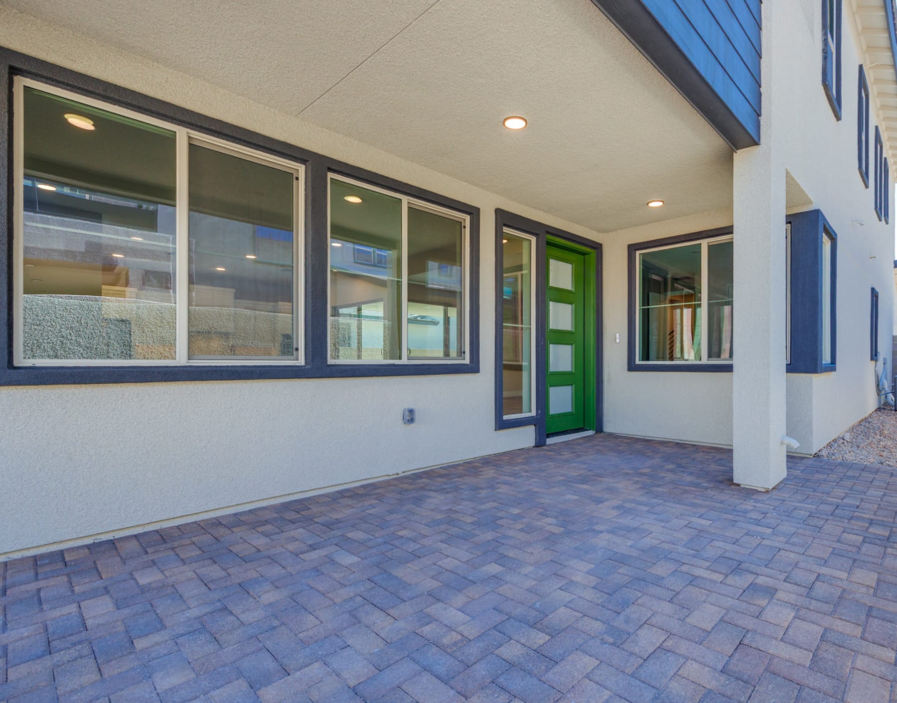 A modern, well-lit building with a paved entrance and large windows, featuring a vibrant green door that stands out against the neutral color scheme.