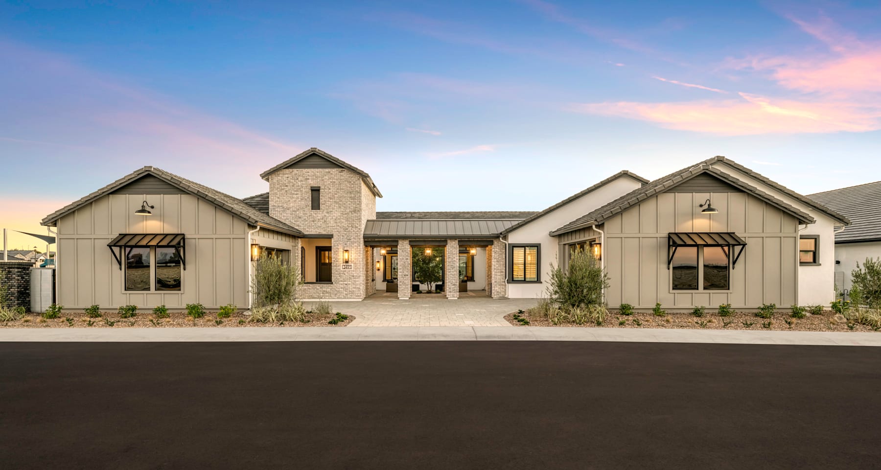 A modern farmhouse-style home with a stone exterior, gabled roofs, and a covered porch sits against a backdrop of a clear blue sky with wispy clouds.