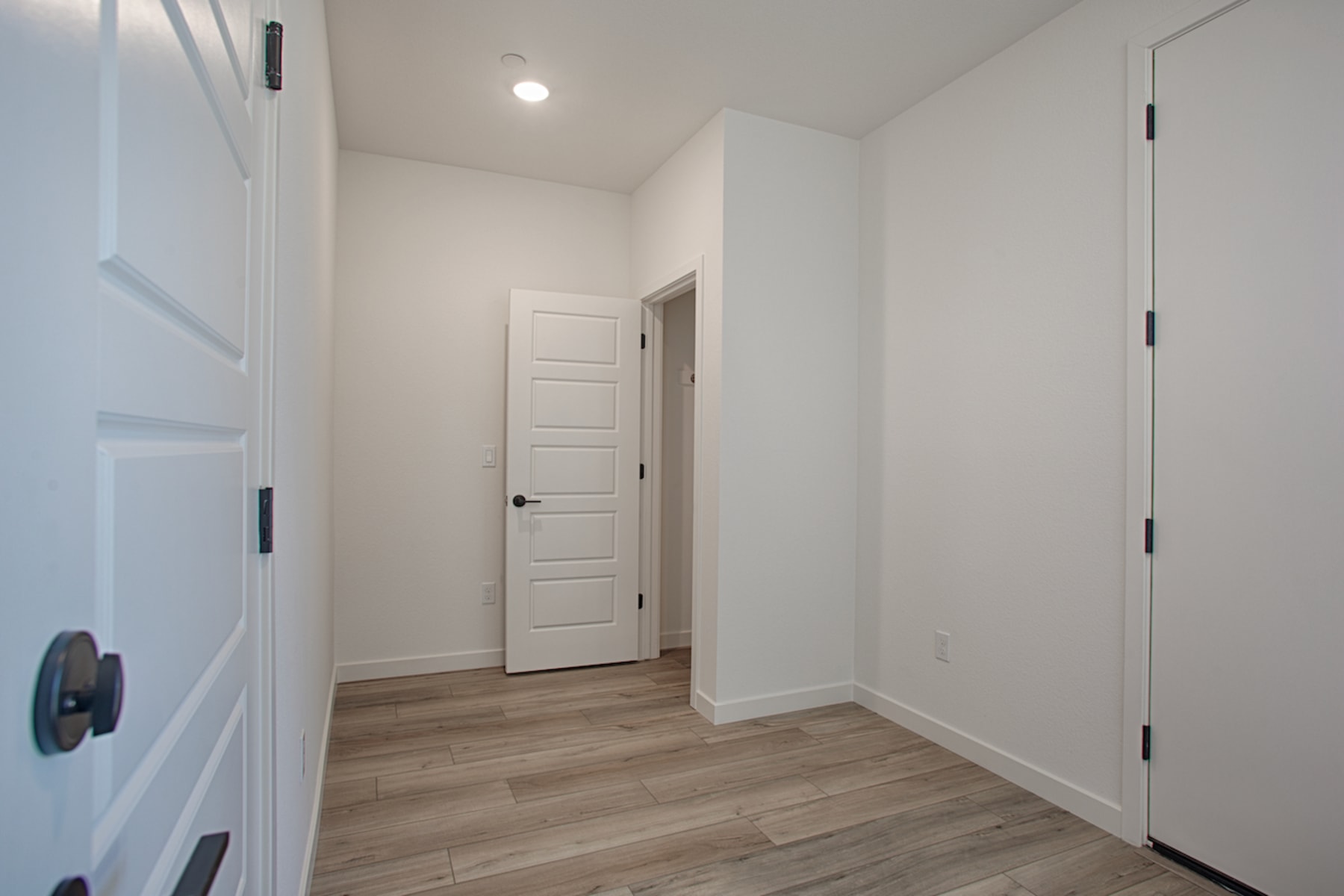 A bright, minimalist hallway with white walls, a wooden floor, and several closed doors leading to other rooms.