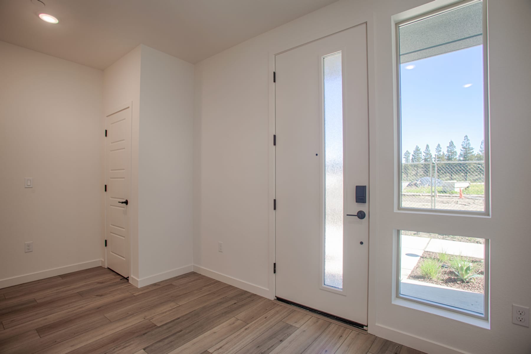 A bright and spacious entryway with a large window overlooking a scenic outdoor landscape, featuring a wooden floor and white walls.