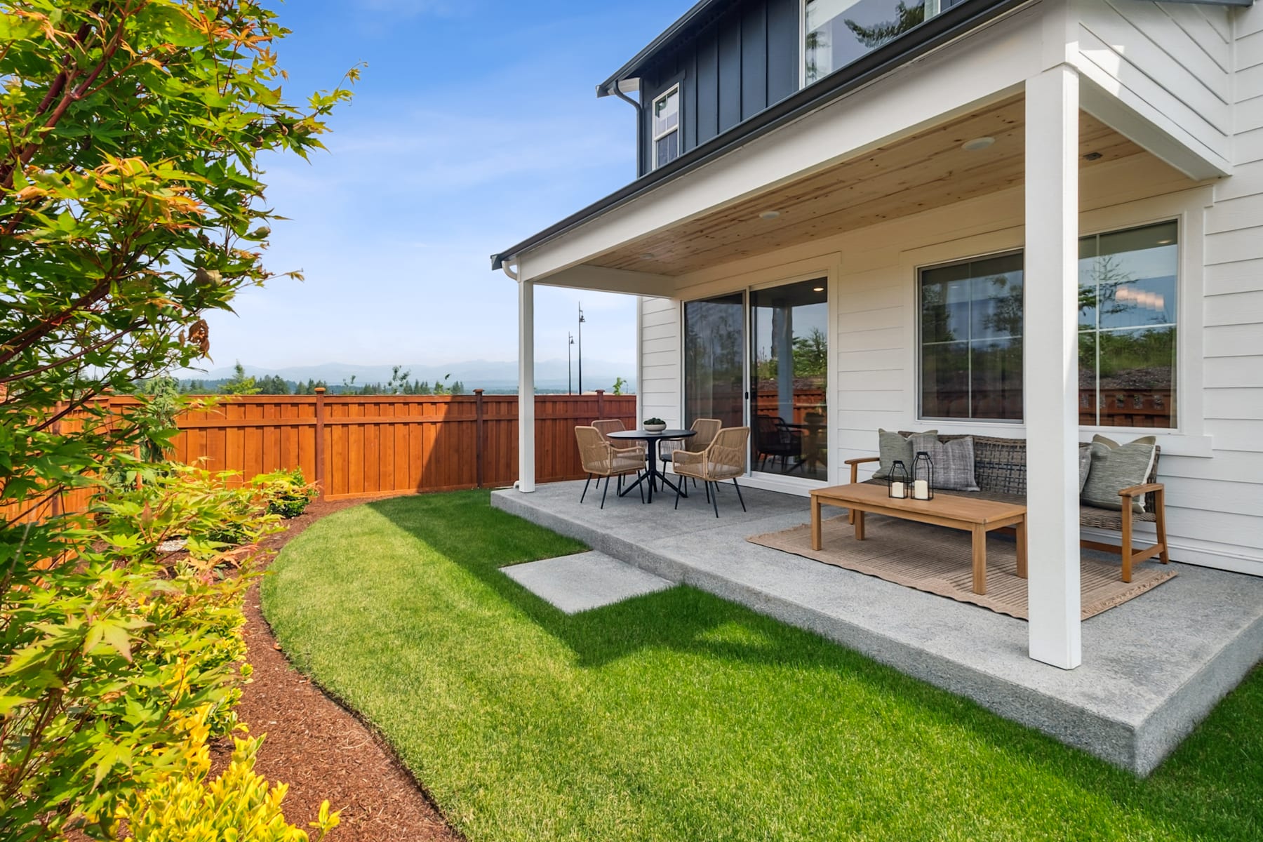 A well-designed backyard with a patio, lush green lawn, and a wooden fence, surrounded by a vibrant garden with colorful foliage.