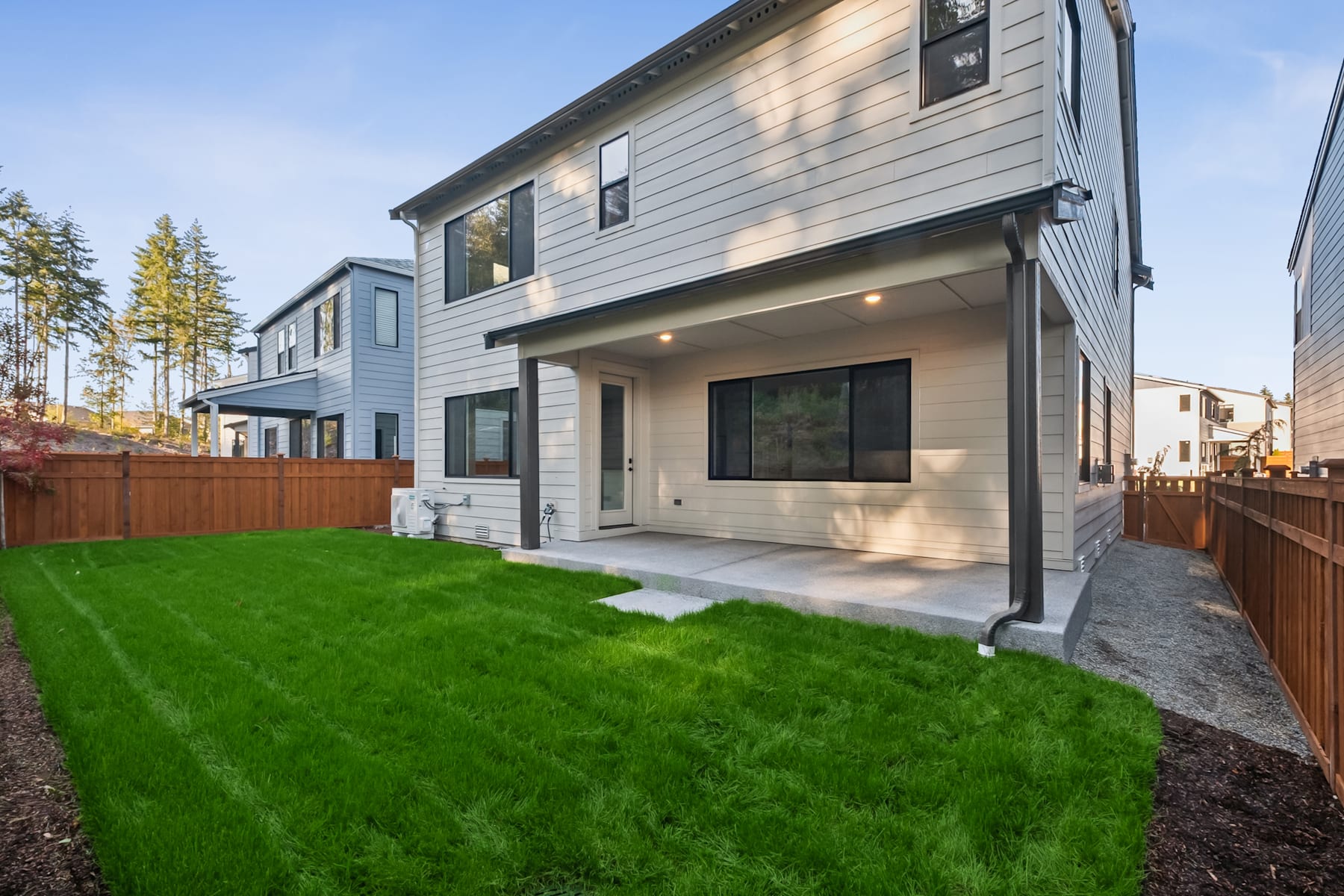 A modern, two-story gray house with a well-manicured lawn and landscaping in the foreground, surrounded by trees in the background.