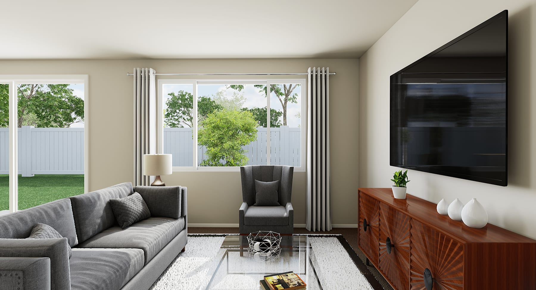 A cozy living room with a gray sofa, a wooden TV stand, and large windows overlooking a lush green outdoor space.