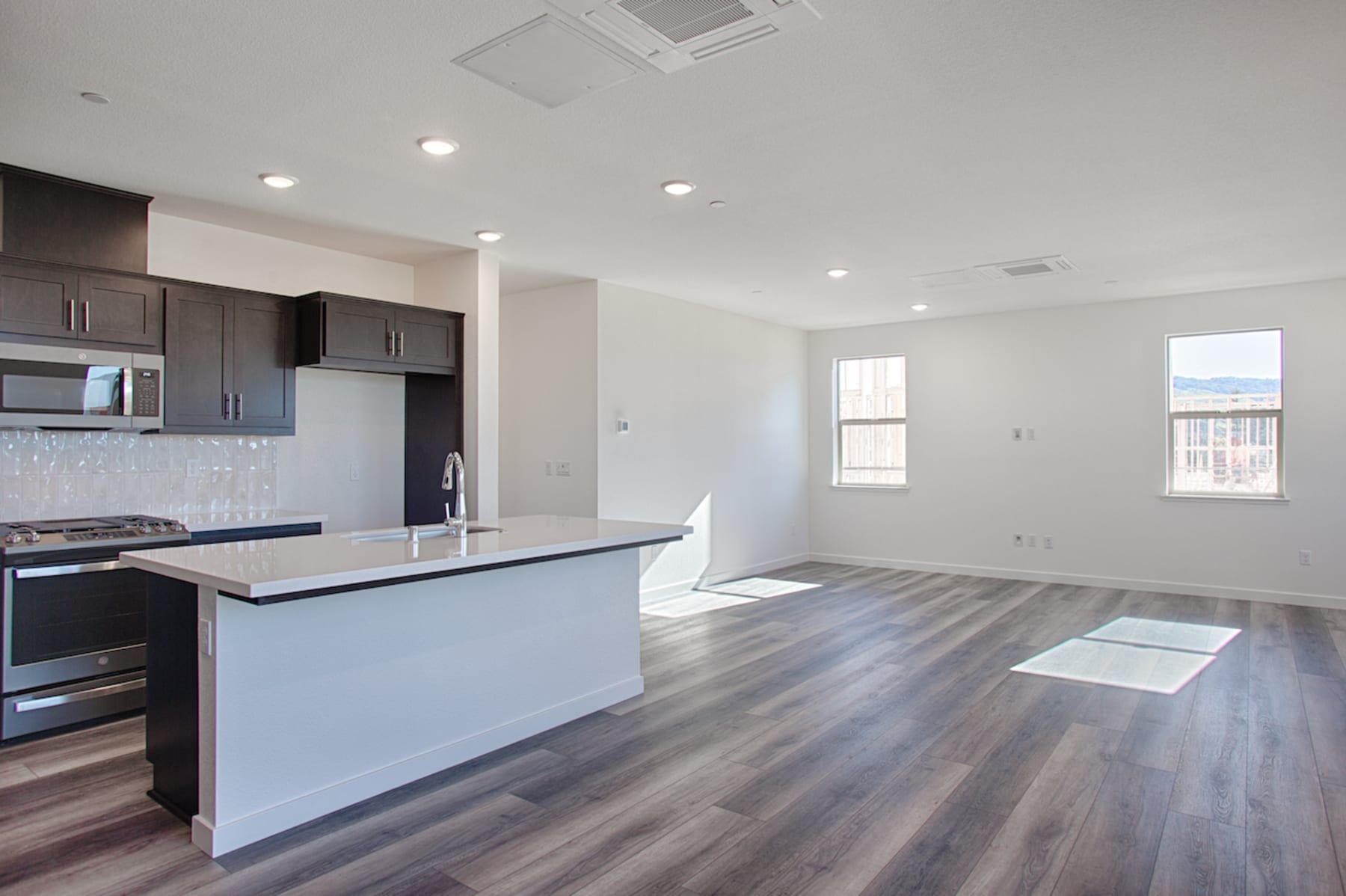 A modern, open-concept kitchen and living room with dark wood cabinets, a white island, and hardwood floors.