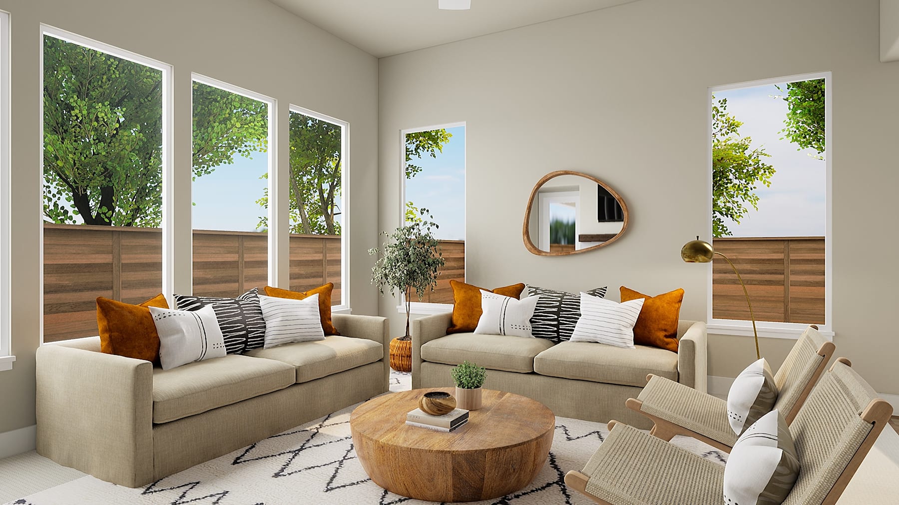 A cozy and inviting living room with large windows overlooking a lush, green outdoor space, featuring a pair of beige sofas adorned with patterned and solid throw pillows, a round wooden coffee table, and a decorative mirror on the wall.
