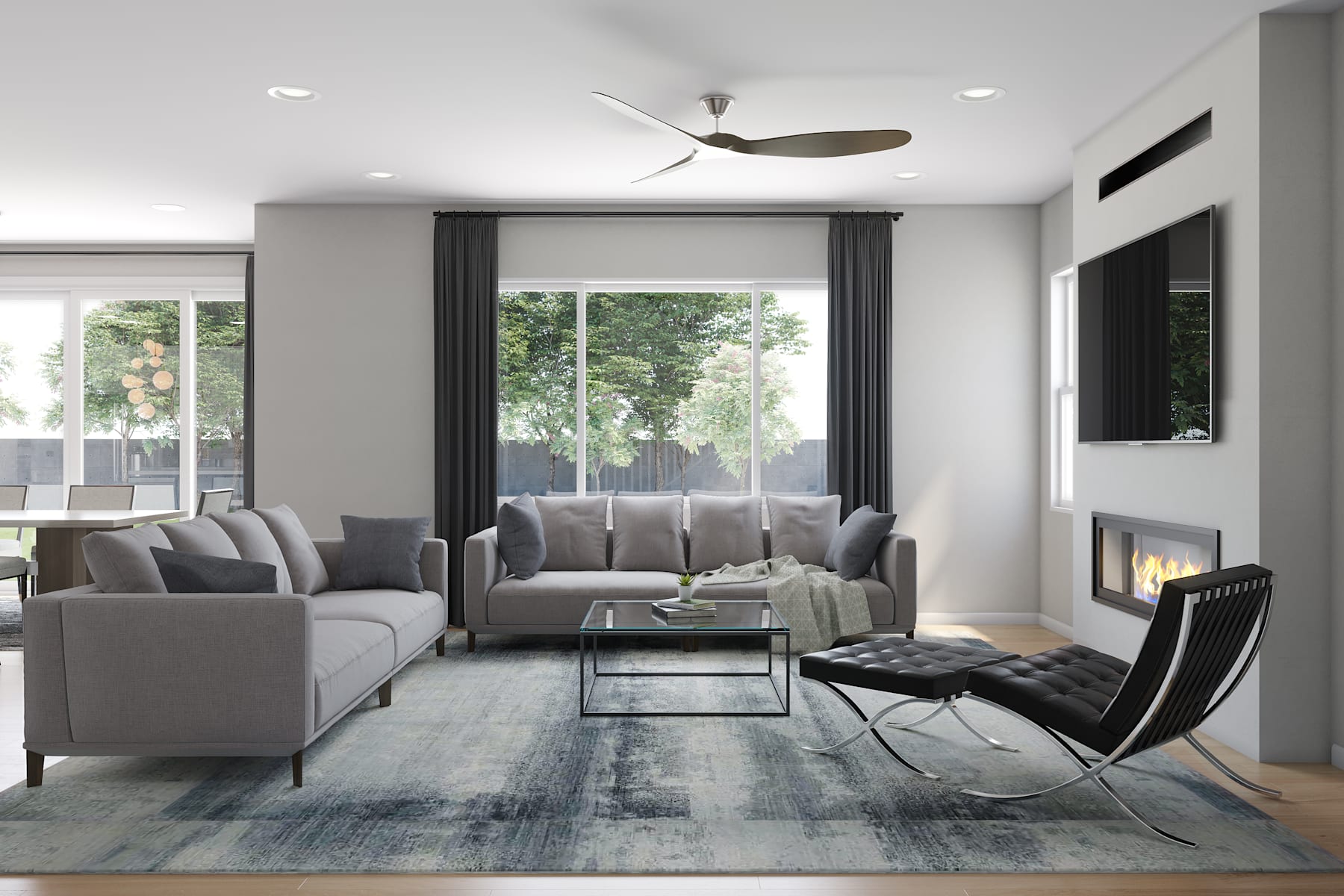A modern and minimalist living room with gray sofas, a glass coffee table, and a Barcelona chair set against a backdrop of large windows overlooking a lush outdoor environment.