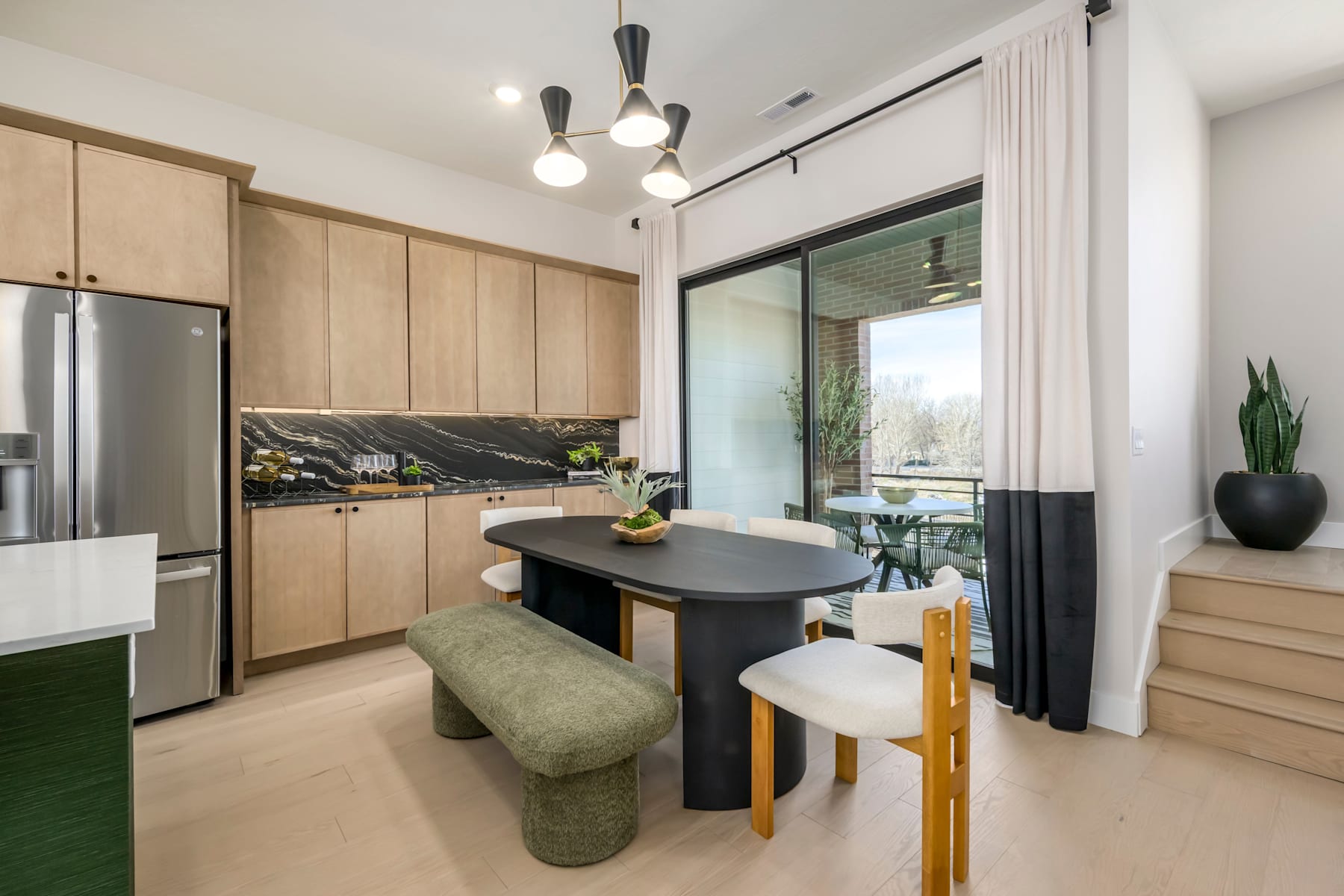 A modern and minimalist kitchen with light wood cabinets, a black island, and a large window overlooking a scenic outdoor view.