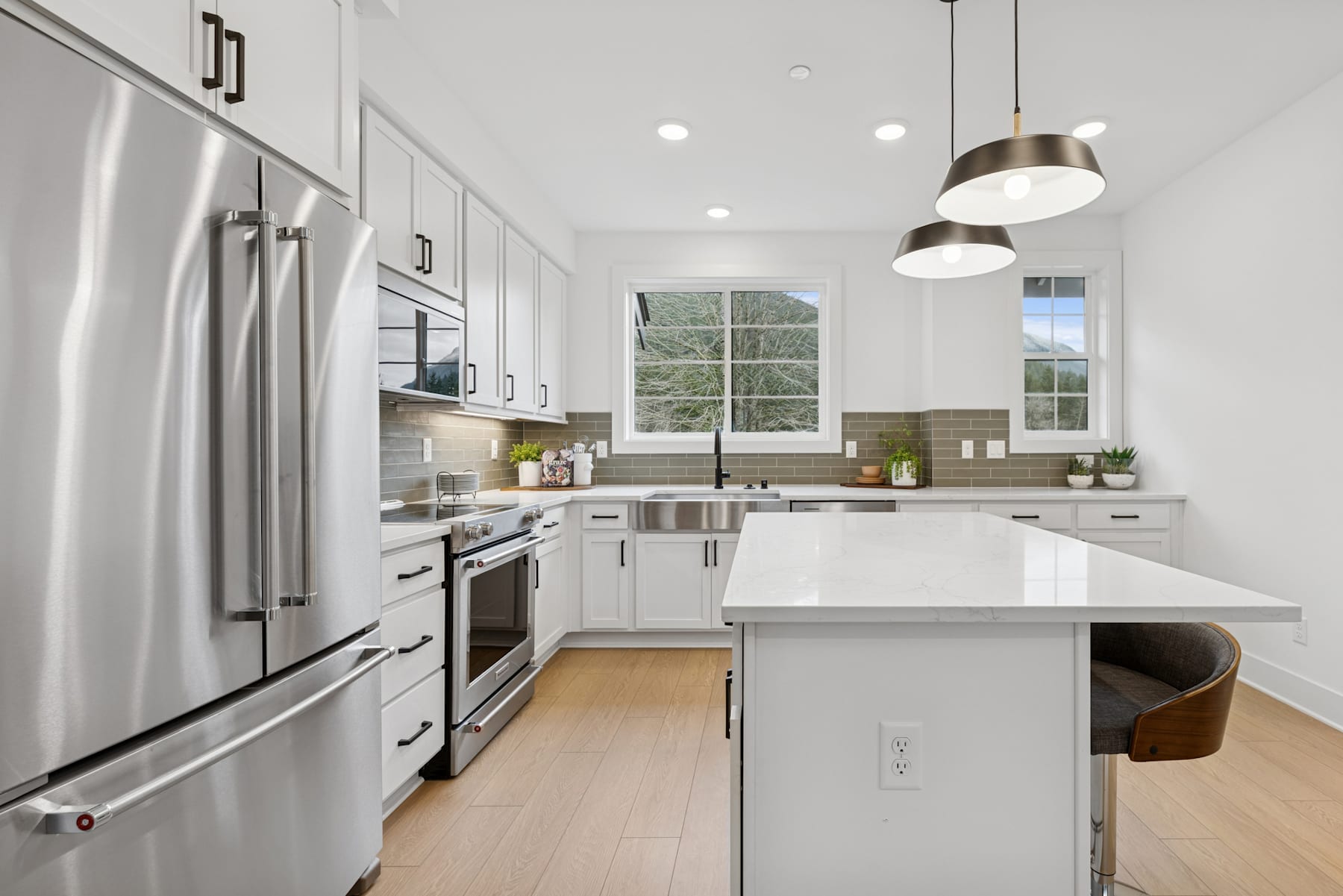A modern, well-lit kitchen with stainless steel appliances, white cabinets, and a central island with a wooden countertop, set against a backdrop of large windows allowing natural light to flood the space.