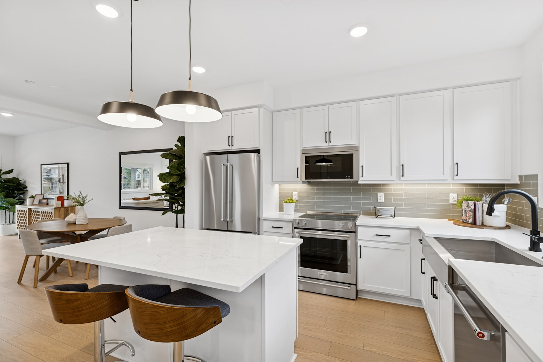 A modern, well-lit kitchen with white cabinets, stainless steel appliances, and a large central island with wooden stools.