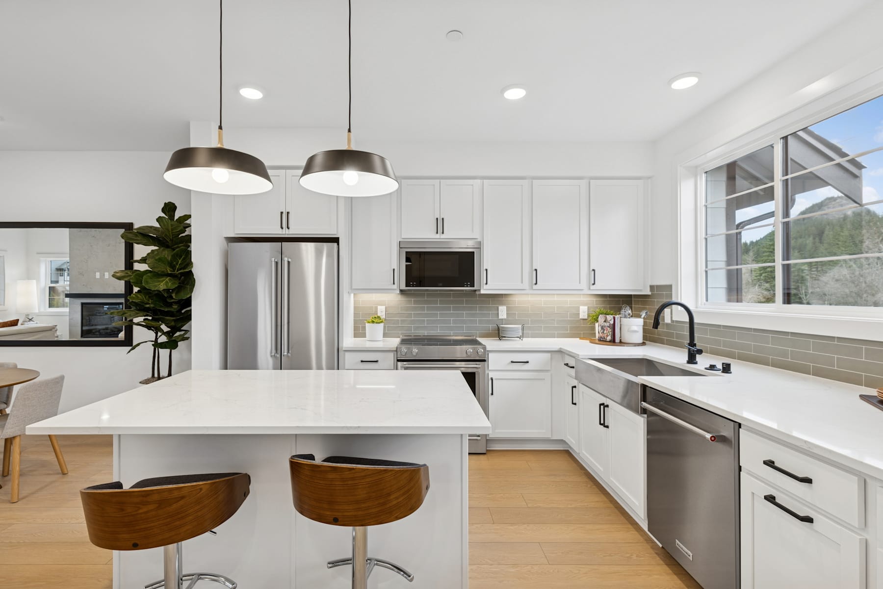 A modern, bright, and spacious kitchen with white cabinets, stainless steel appliances, a large island with wooden stools, and pendant lights illuminating the space.