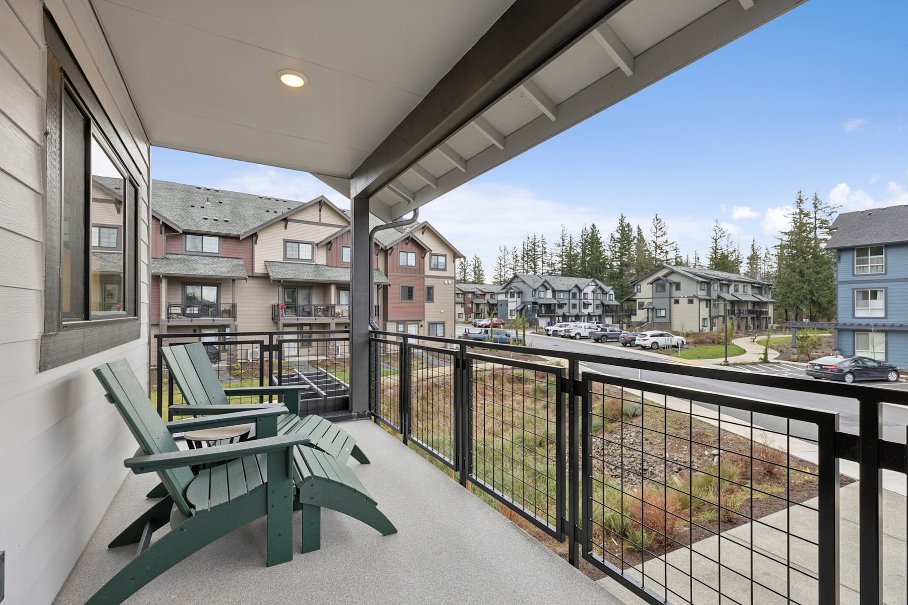 The image shows a balcony with a metal railing overlooking a residential neighborhood with several multi-story buildings and trees in the background.