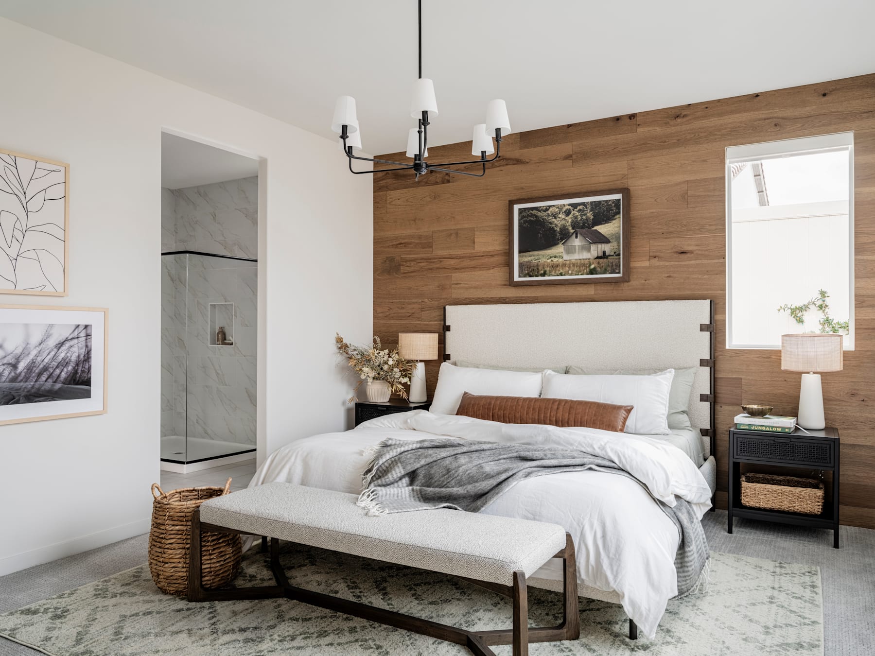 A cozy and inviting bedroom with a wooden accent wall, a plush bed with neutral bedding, and various decorative elements such as artwork, lamps, and a bench at the foot of the bed.