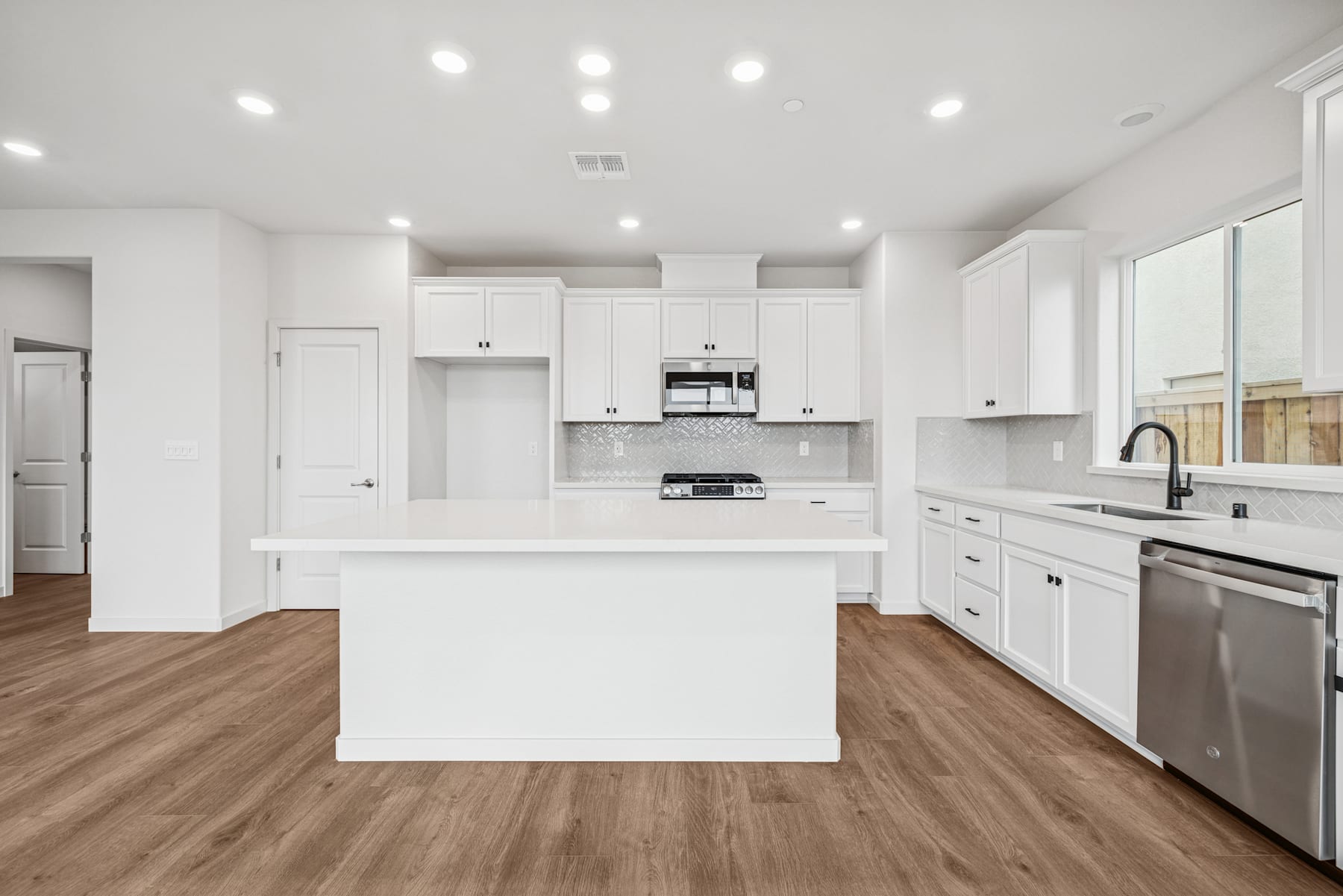 A modern, bright, and spacious kitchen with white cabinets, stainless steel appliances, and a large central island with a wooden floor.