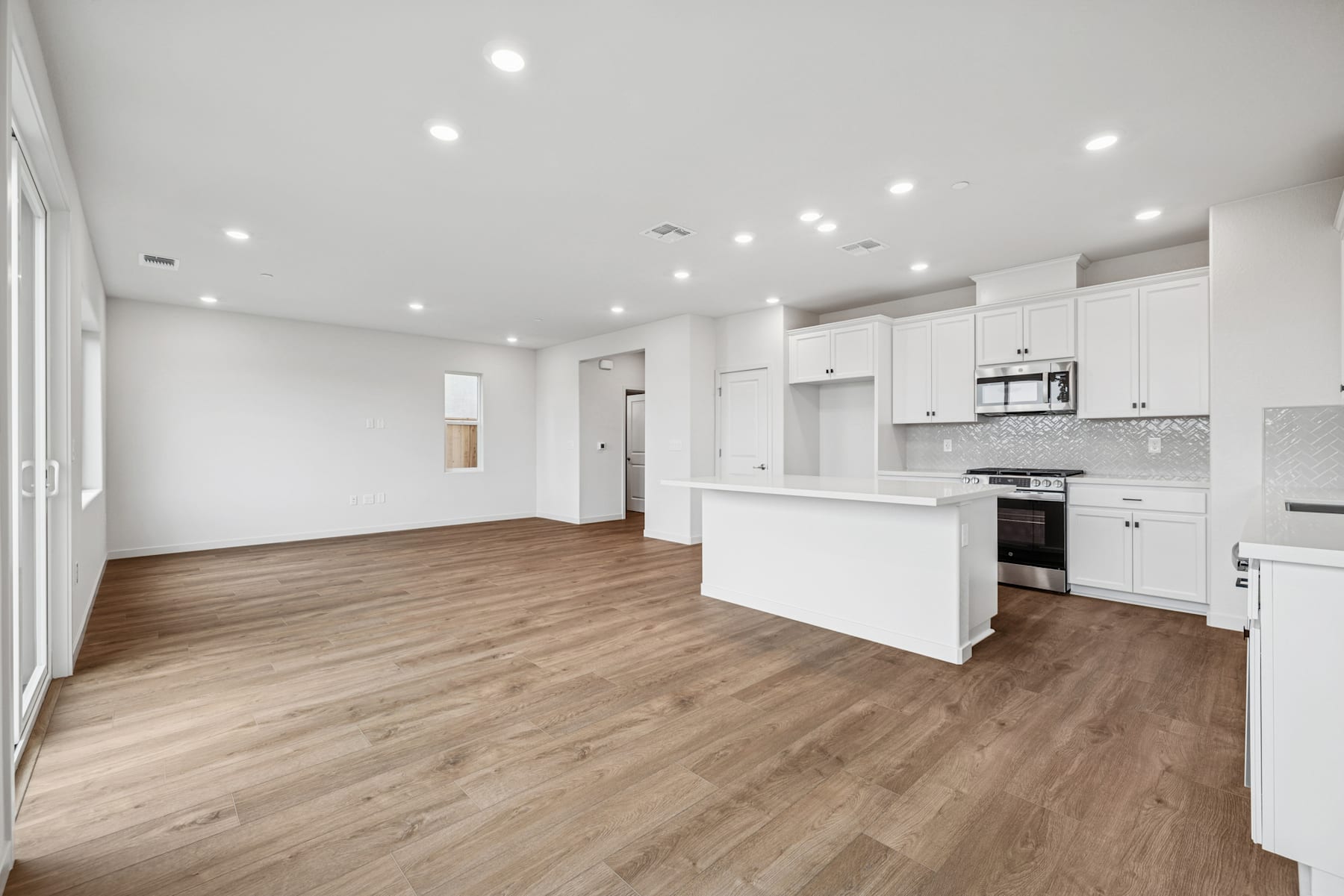 A spacious, modern kitchen and living room with white cabinets, hardwood floors, and recessed lighting.