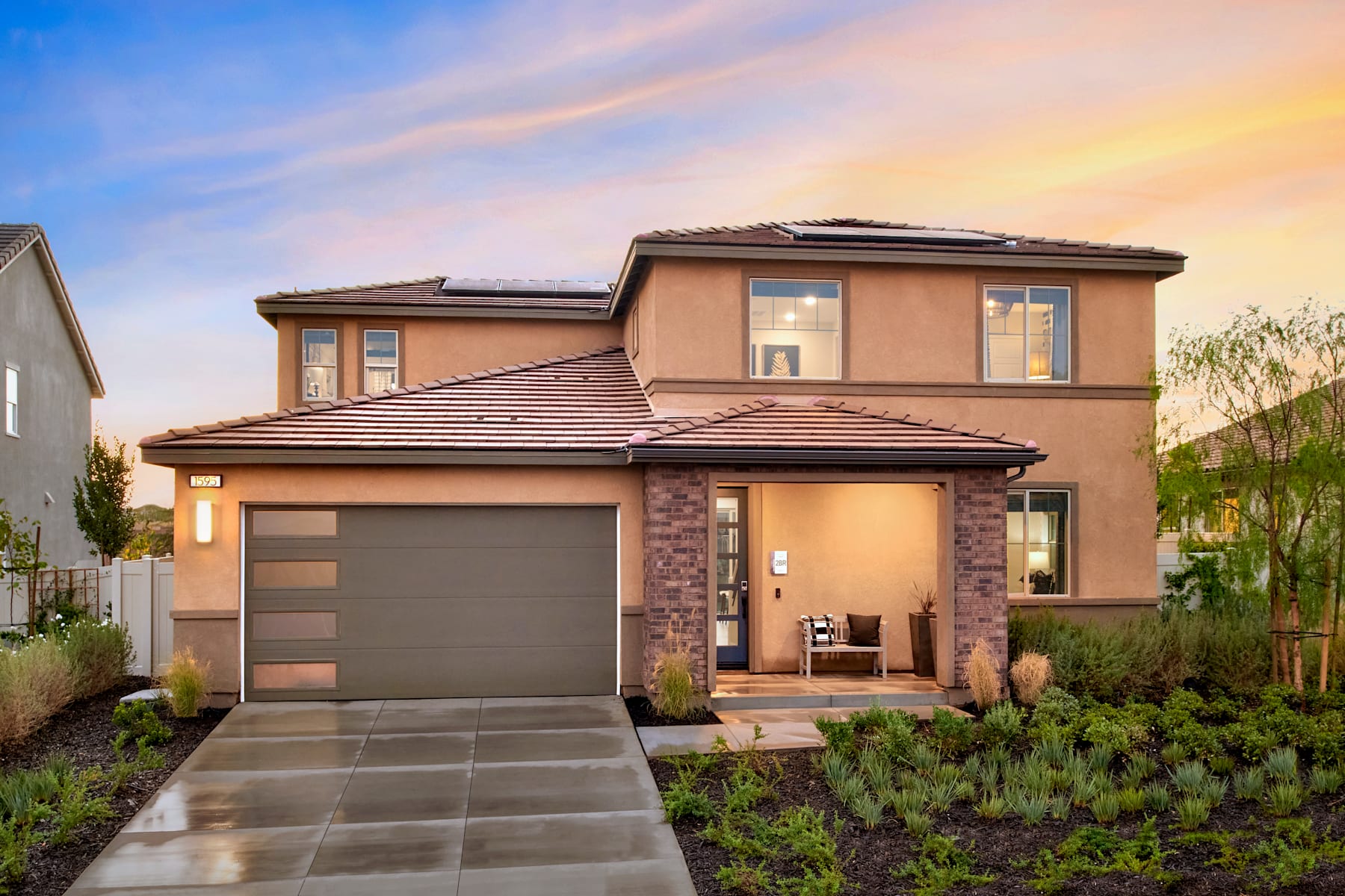 A two-story residential house with a garage, surrounded by a well-maintained landscaped yard, set against a vibrant sunset sky.