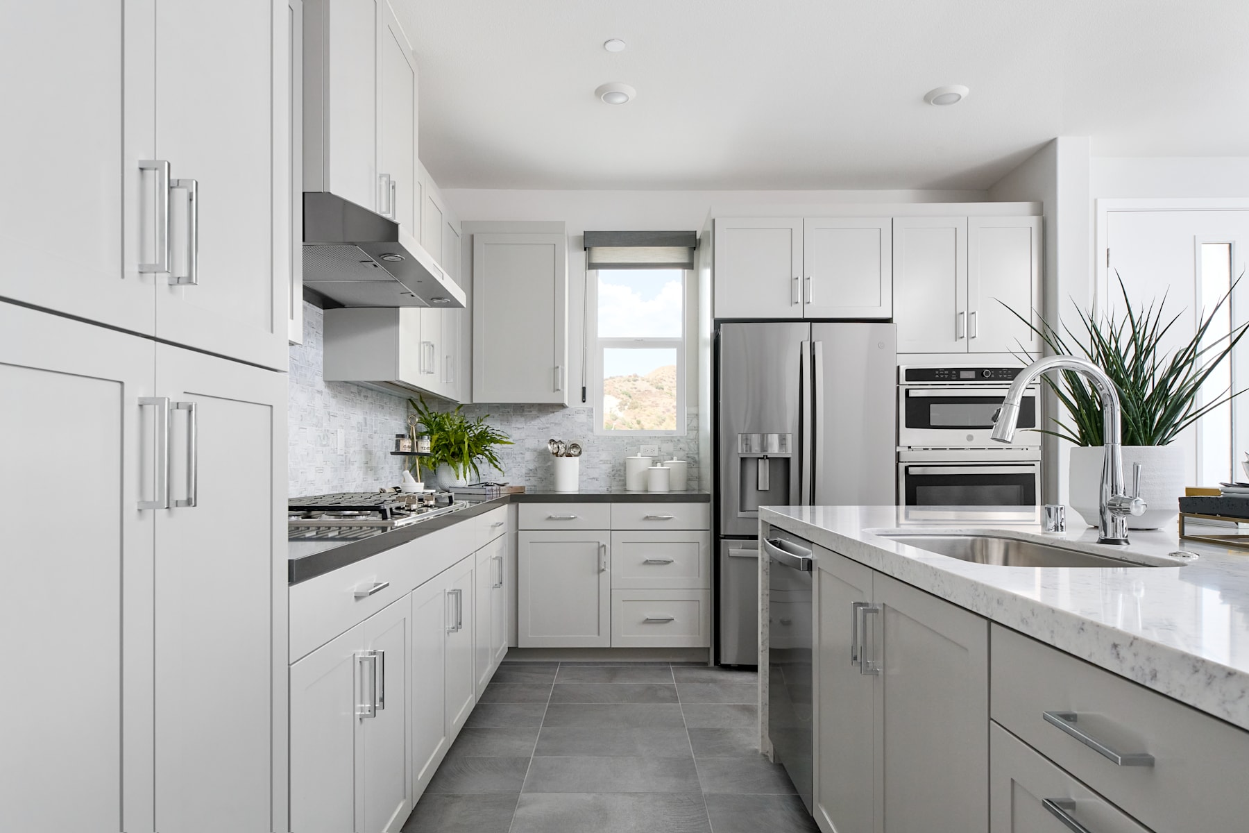 A modern, well-equipped kitchen with white cabinets, stainless steel appliances, and a central island with a marble countertop.