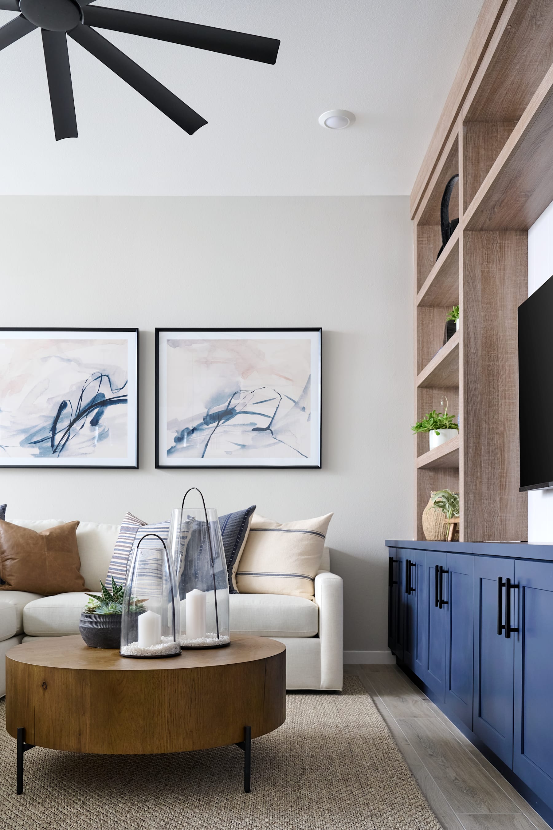 A modern and cozy living room with a large ceiling fan, framed abstract art, a wooden coffee table, and a blue storage cabinet in the background.